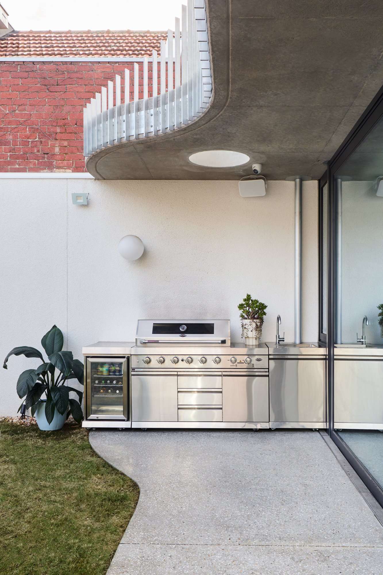 Park St by SGKS ARCH. Photography by Tania Lee. Backyard with concrete patio with stainless steel joinery and barbeque alongside grass.