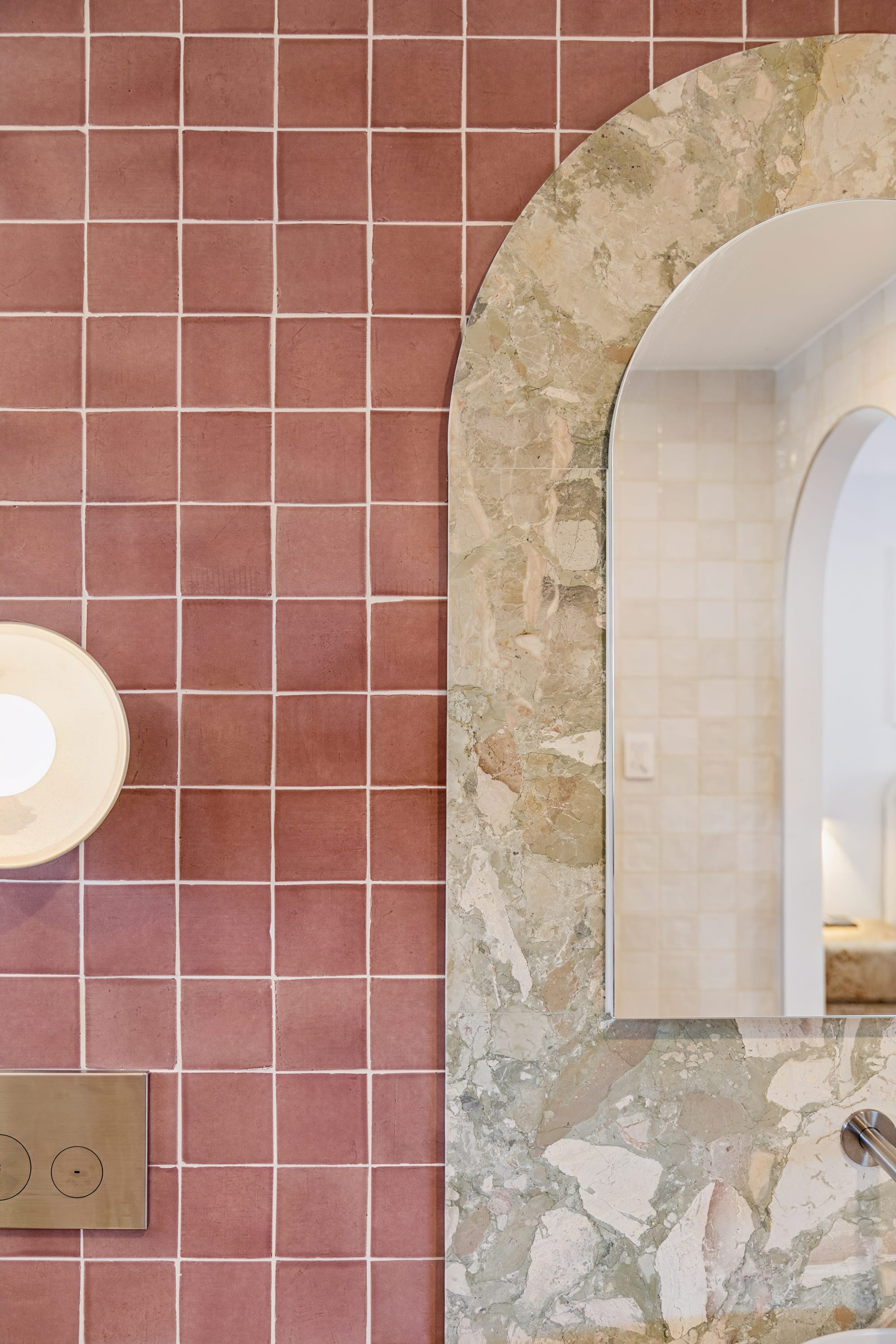 Chardonnay Court House by Studio MDM. Photography by Focl Media. Close up of bathroom wall showing pink wall tiles meeting arched light green stone splashback and arched mirror. 