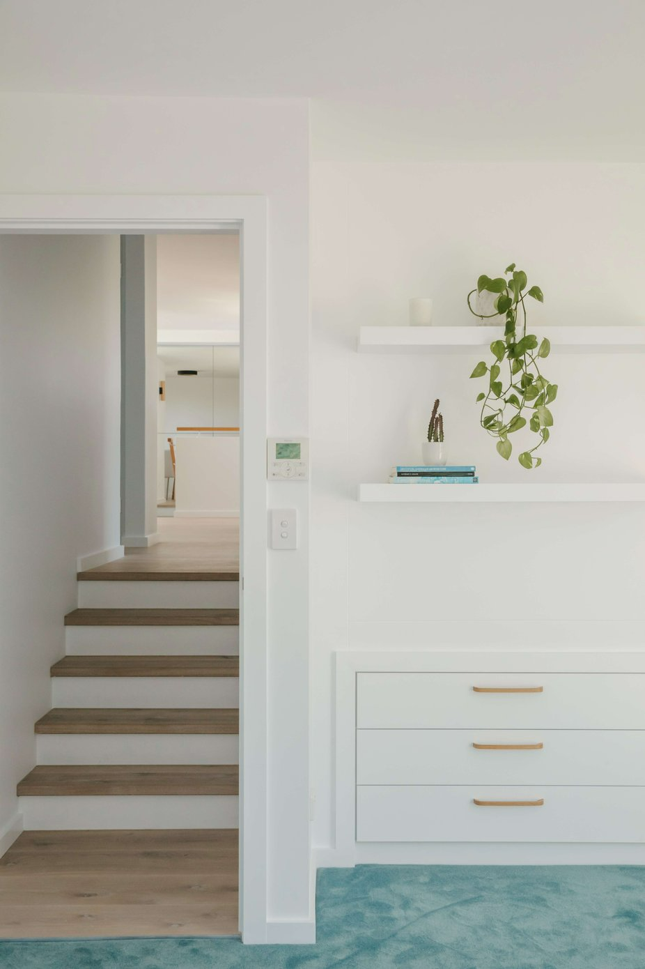 Westleigh Wonder by Nathalie Scipioni Architects. Photography by Alexandra Adoncello. Timber stairs running alongside room with blue carpets and white cabinetry.