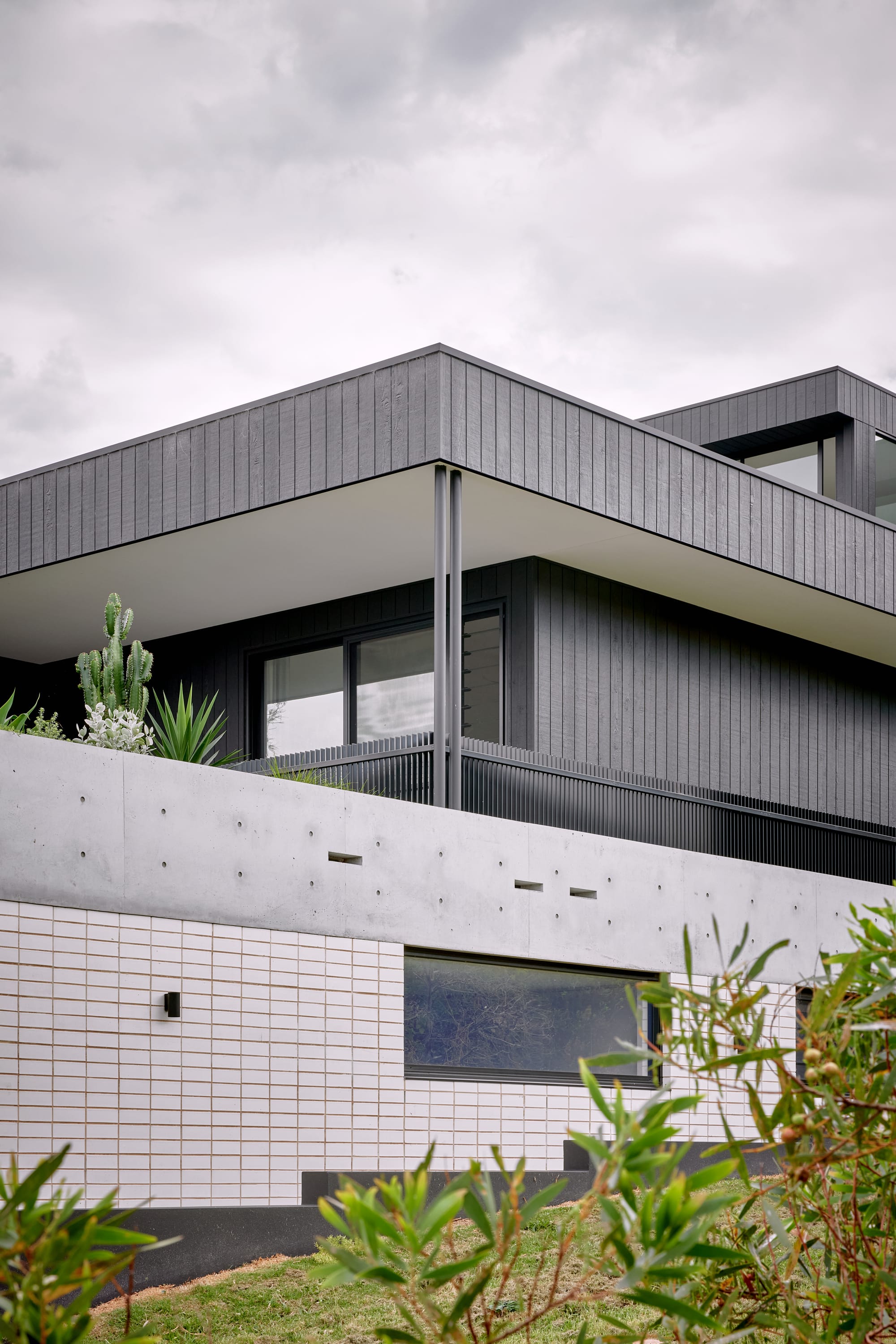 Headland House by Baikie Corr Architecture. Photography by Toby Peet. Exterior facade of multi-level home with white brick, concrete black timber cladding and back balustrade along the balcony. 