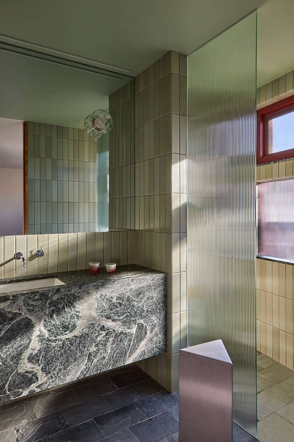An interior of a modern bathroom with marble, green and slate tiles with a fluted glass screen.