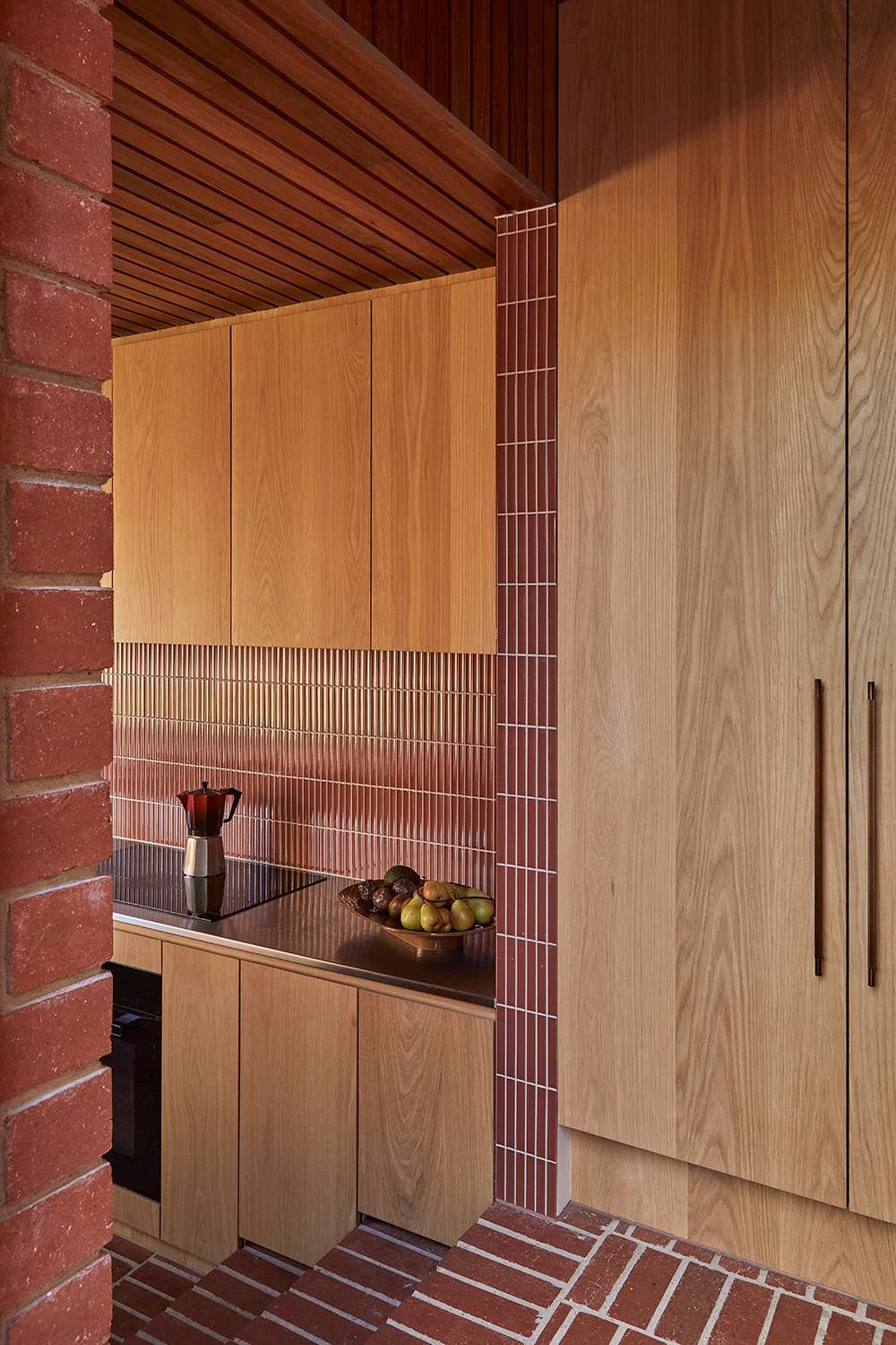 An interior detail shot of a kitchen with timber veneer and terracotta tiles.