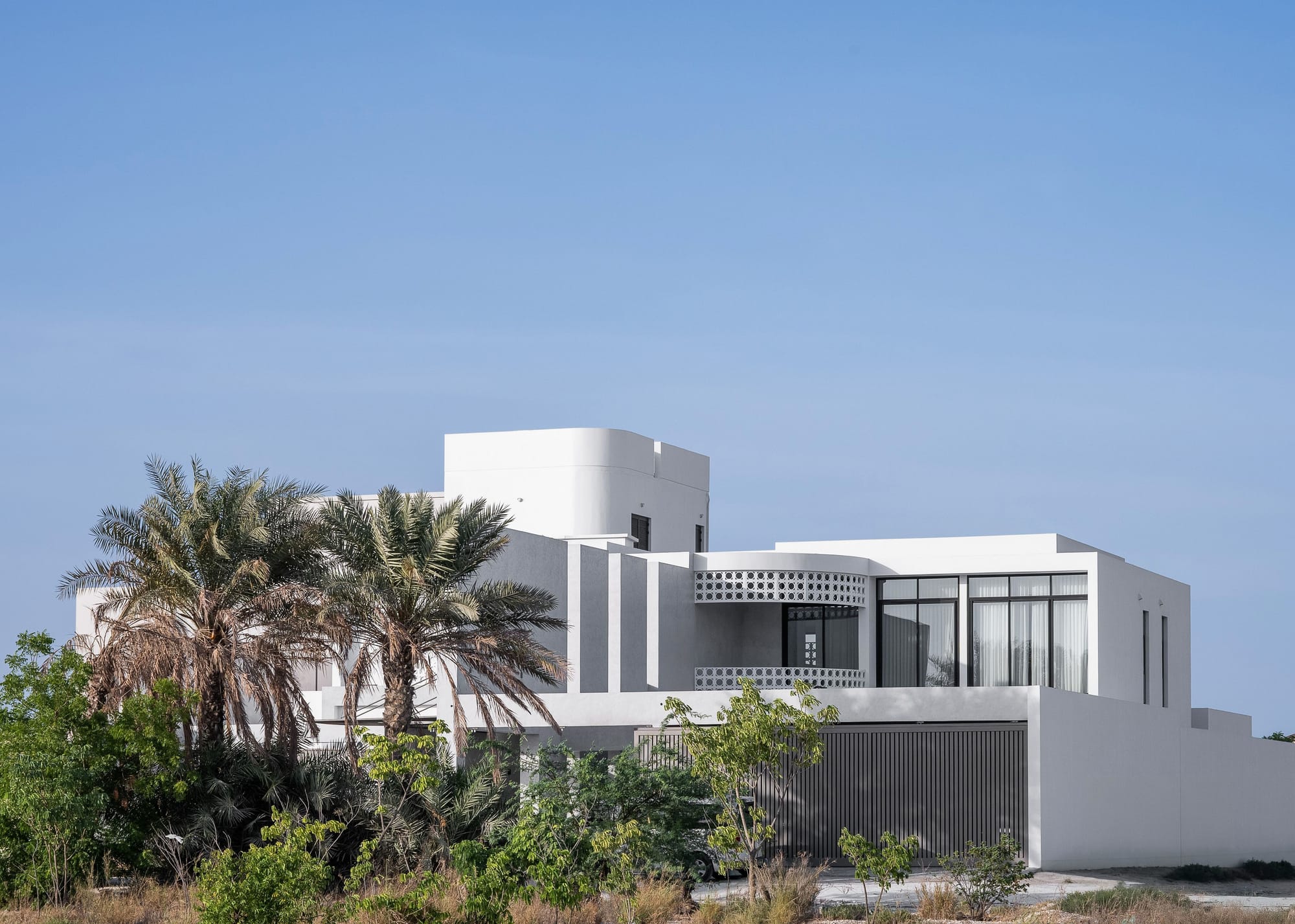 Veil House by ENCLAVE Architects. Photography by Hassan Arante & Gener Rayes. Facade of multistorey contemporary home with decorative screening, white facade and palm trees.