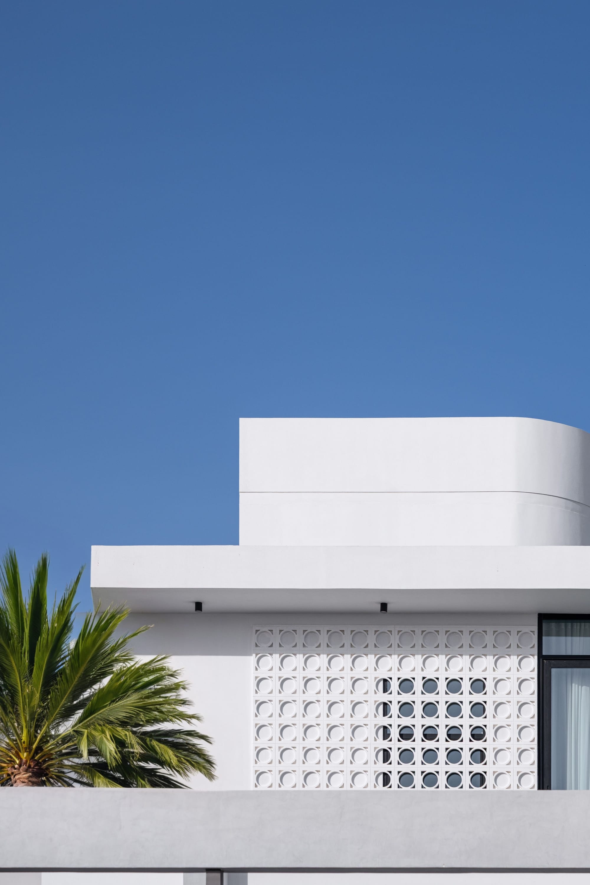 Veil House by ENCLAVE Architects. Photography by Hassan Arante & Gener Rayes. Exterior facae of white home, double storey contemporary home with decorative screening and palm trees.