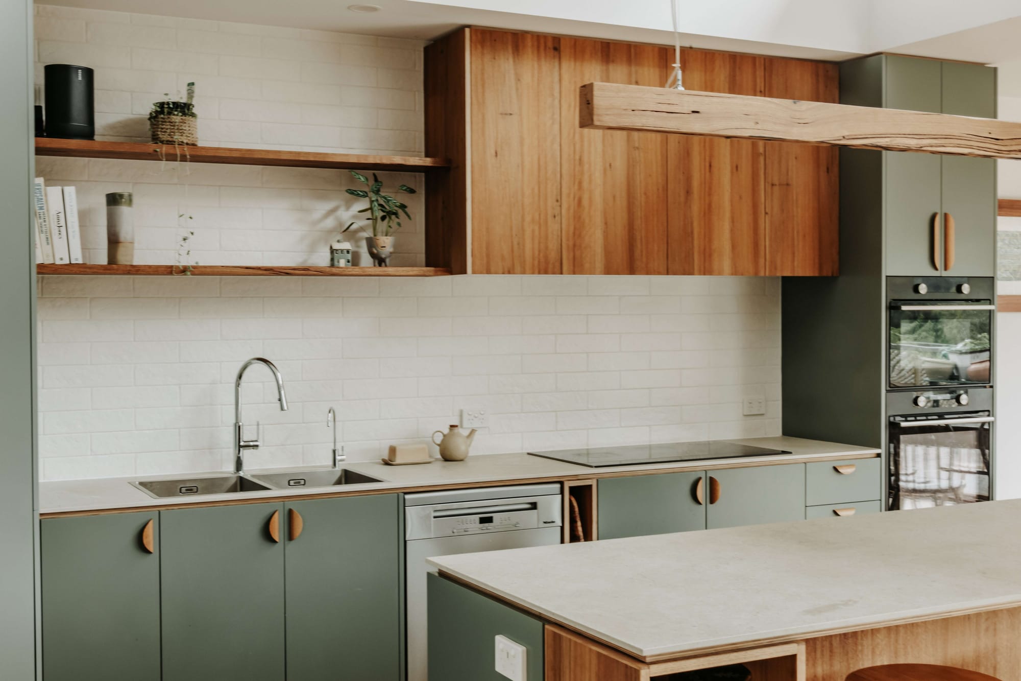 An interior shot of the kitchen at Hemp Home showing the green cabinetry and timber veneer.