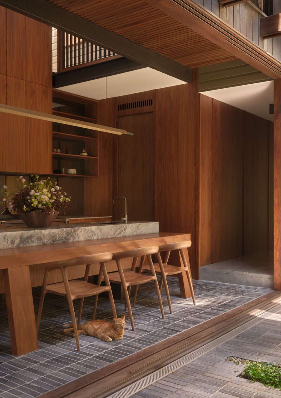 An image of the timber kitchen with a marble island bench and a timber bench for dining in the forground.