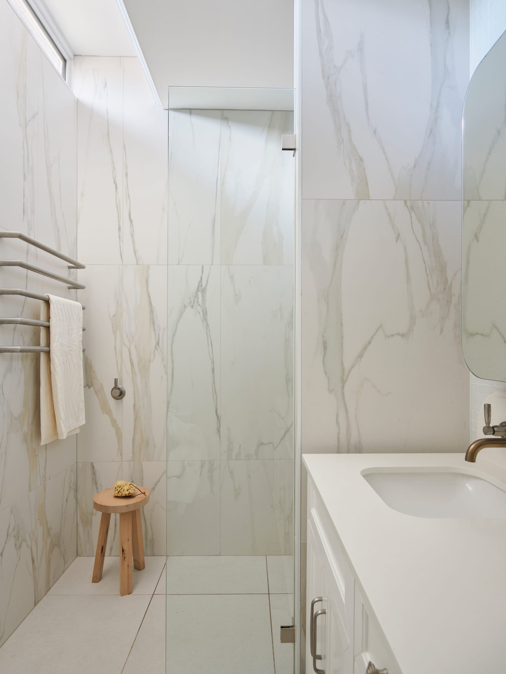 The Darling Edit by Marylou Sobel Interior Design. Photography by Anson Smart. Bathroom with white tiled stone walls, glass shower screen, wooden stool and white vanity.