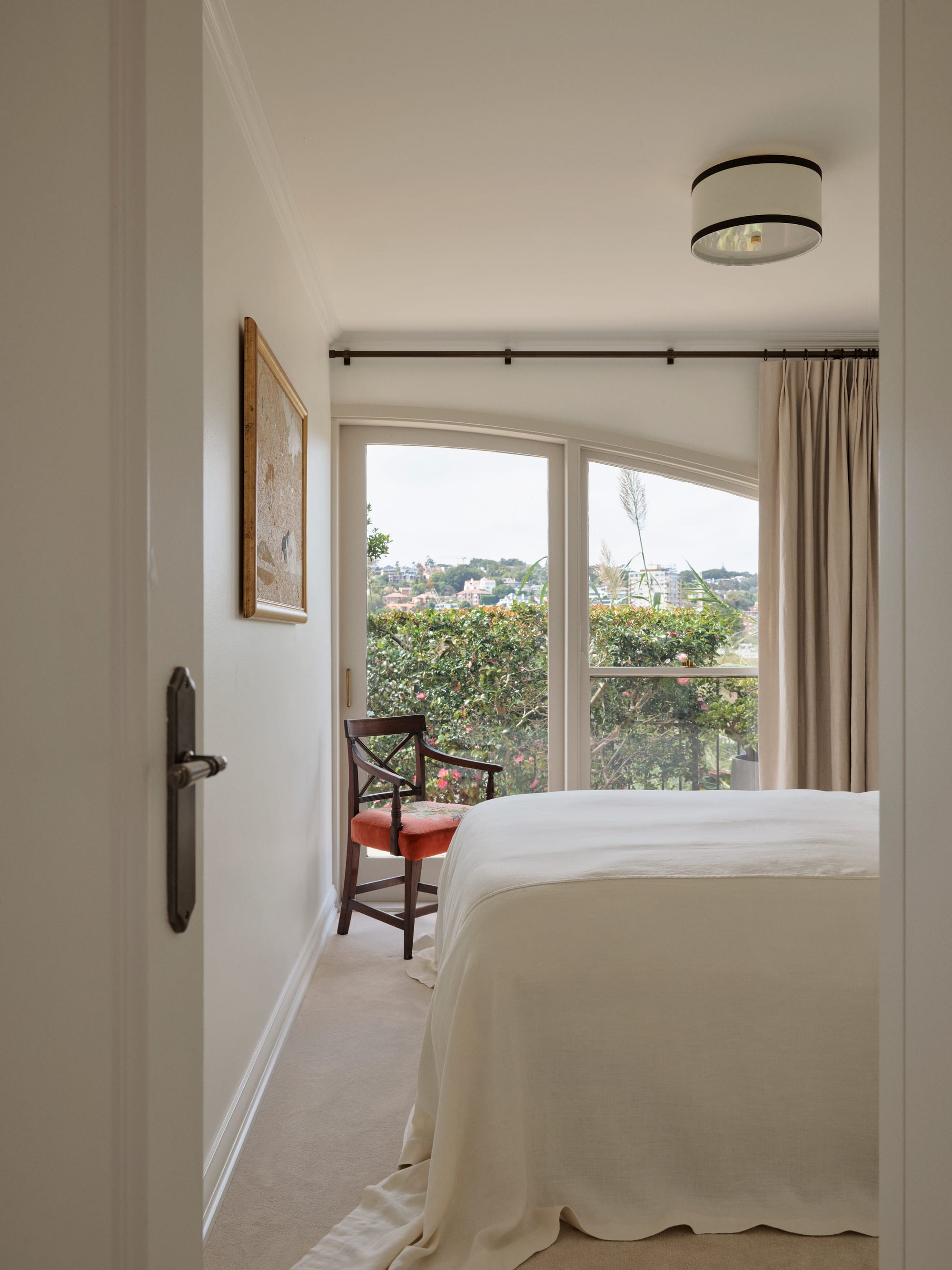 The Darling Edit by Marylou Sobel Interior Design. Photography by Anson Smart. Bedroom with light carpets, a vintage armchair and a window overlooking garden.