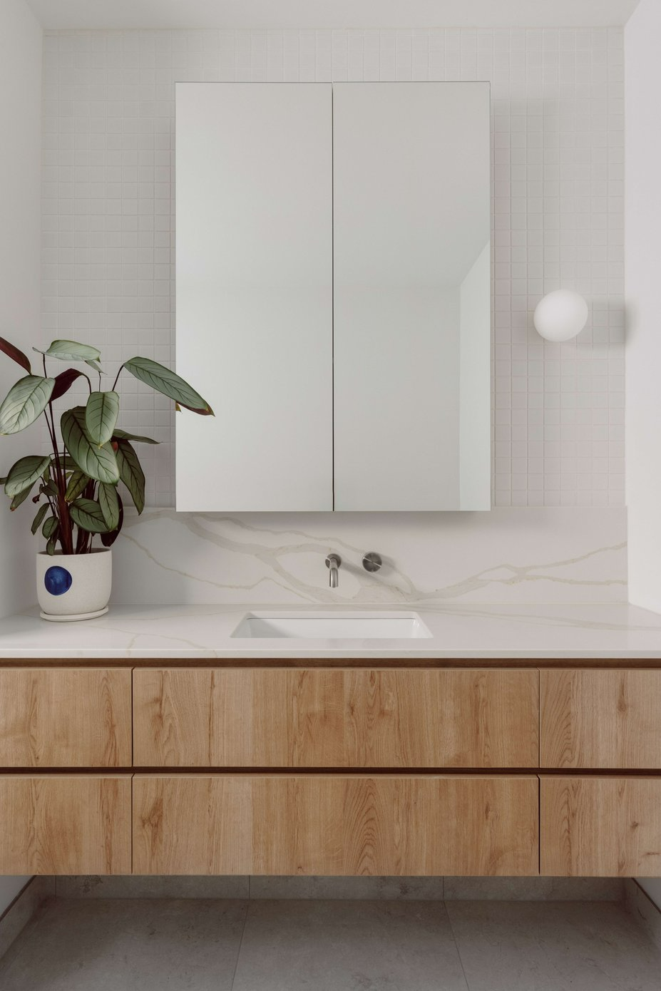 MAUD by Mancini Made. Photography by Elise Scott. Bathroom with floating timber cabinet, with white stone countertop and splashback, floating mirrored cabinet and white mosaic wall tile. 