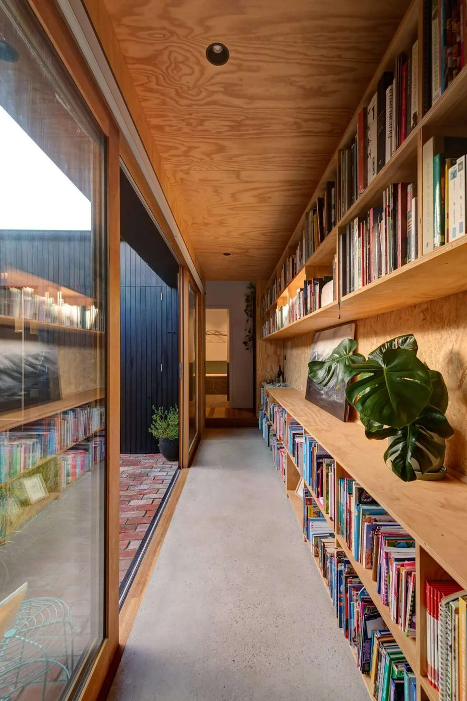 237 York Street, South Melbourne by Plico Design Studio. Photography by Jamie Diaz Berrio. Hallway with concrete floors, sliding timber-framed glass doors and plywood bookshelf on the right. 