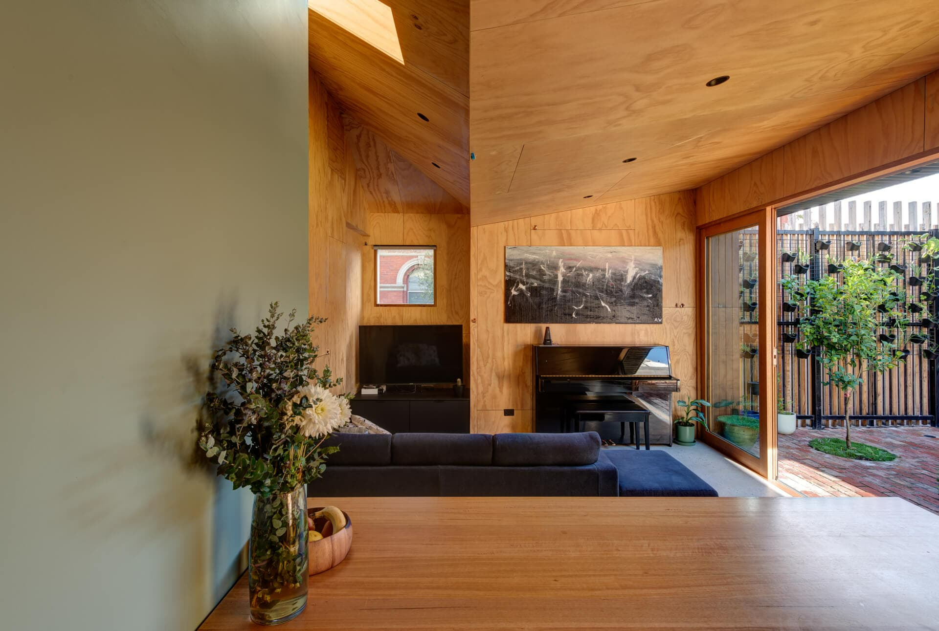 237 York Street, South Melbourne by Plico Design Studio. Photography by Jamie Diaz Berrio. Living space with angular plywood ceiling, plywood walls and sliding glass doors opening onto paved courtyard. 