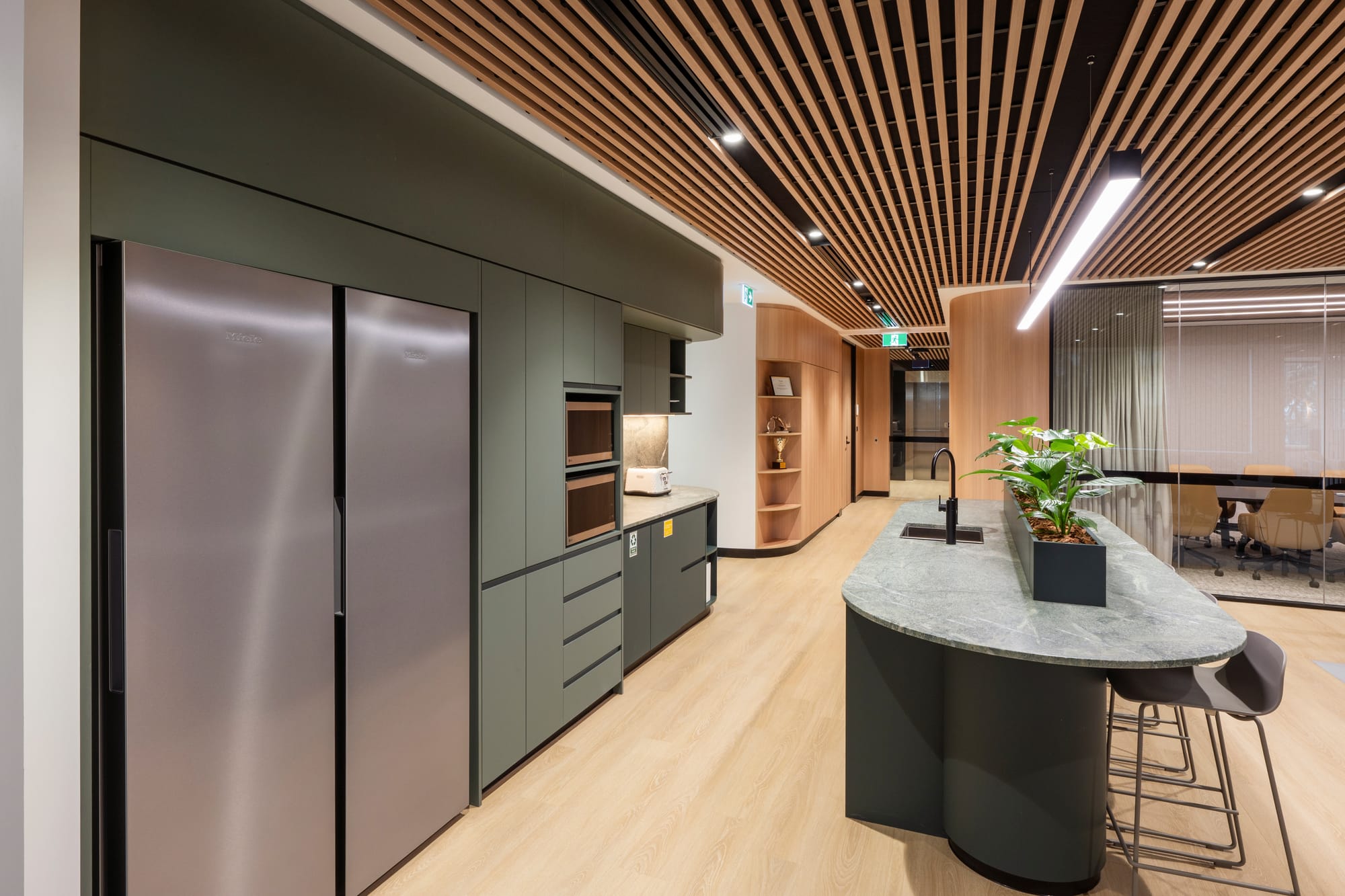 MDA National by Saru Design. Photography by Pete Battye. Kitchen space in office setting, with green cabinets, light timber floors and black island bench with stone countertop. 
