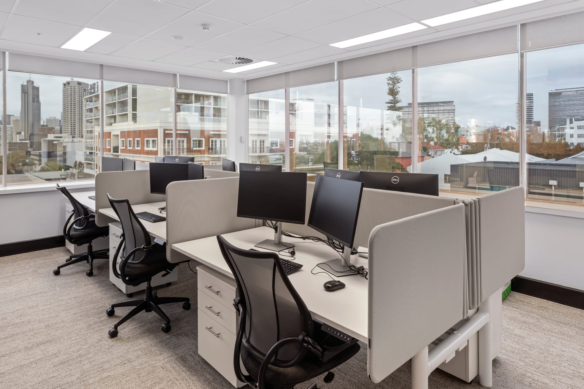 MDA National by Saru Design. Photography by Pete Battye. Booth desks in office space with city views, grey carpeted flooring and white ceiling. 