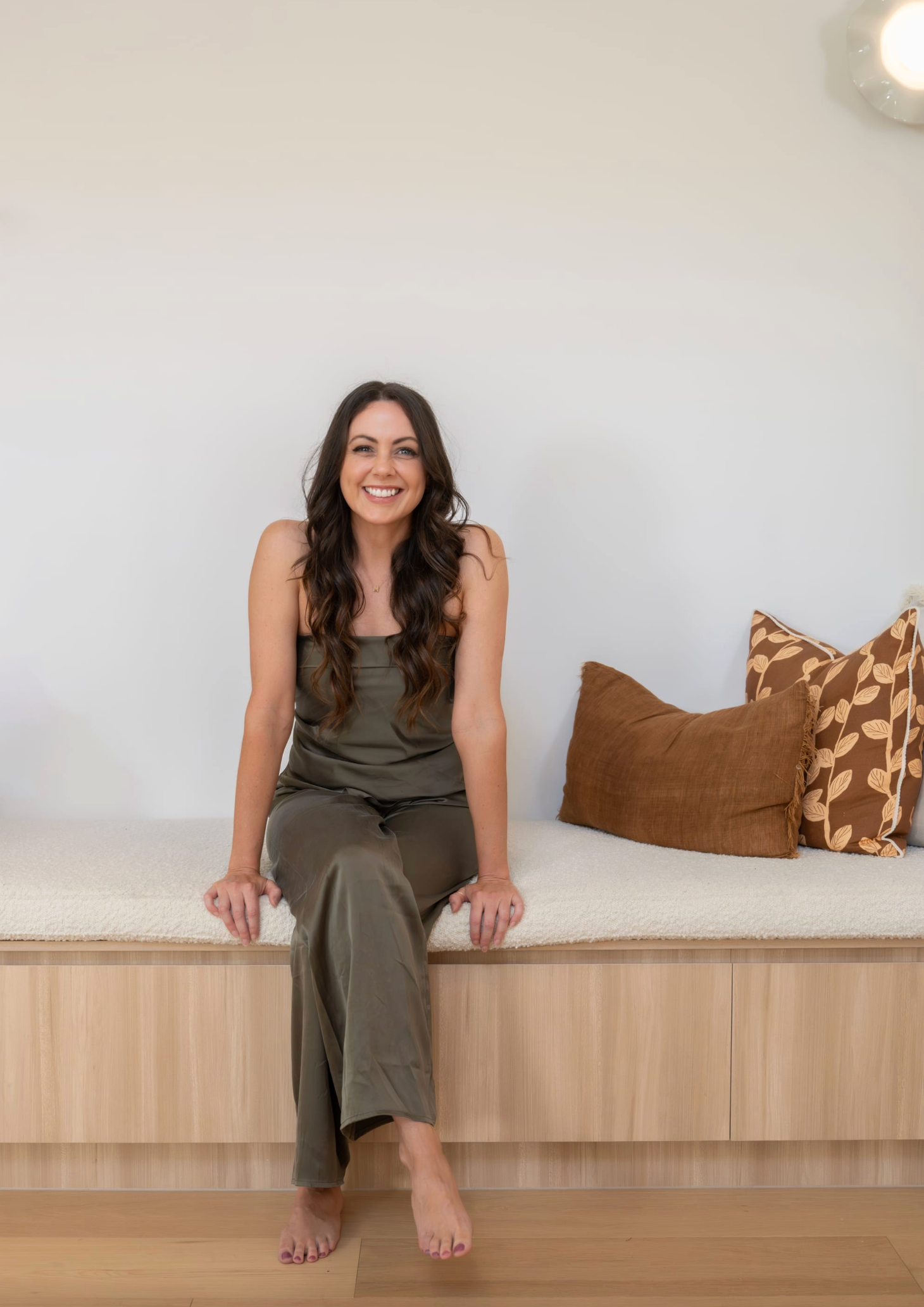 Mel McKoy of Studio MDM. Photography by Focl Media. Woman in olive satin set sitting on timber bench. 
