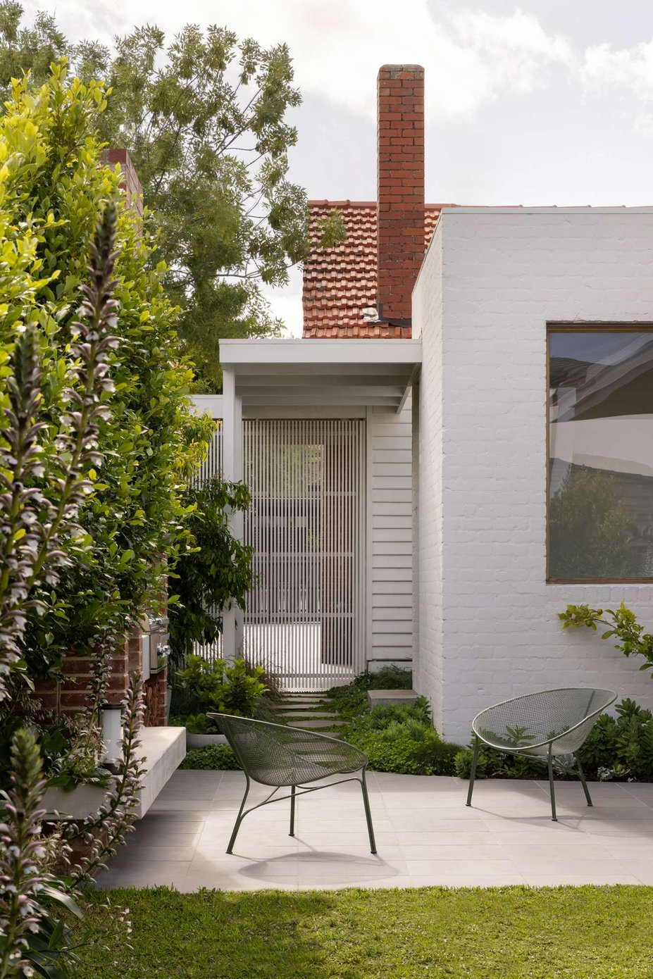 Ormond by Telha Clarke. Photography by Tim Kaye. Rear facade of white brick home with paved exterior sitting area and grass backyard. 