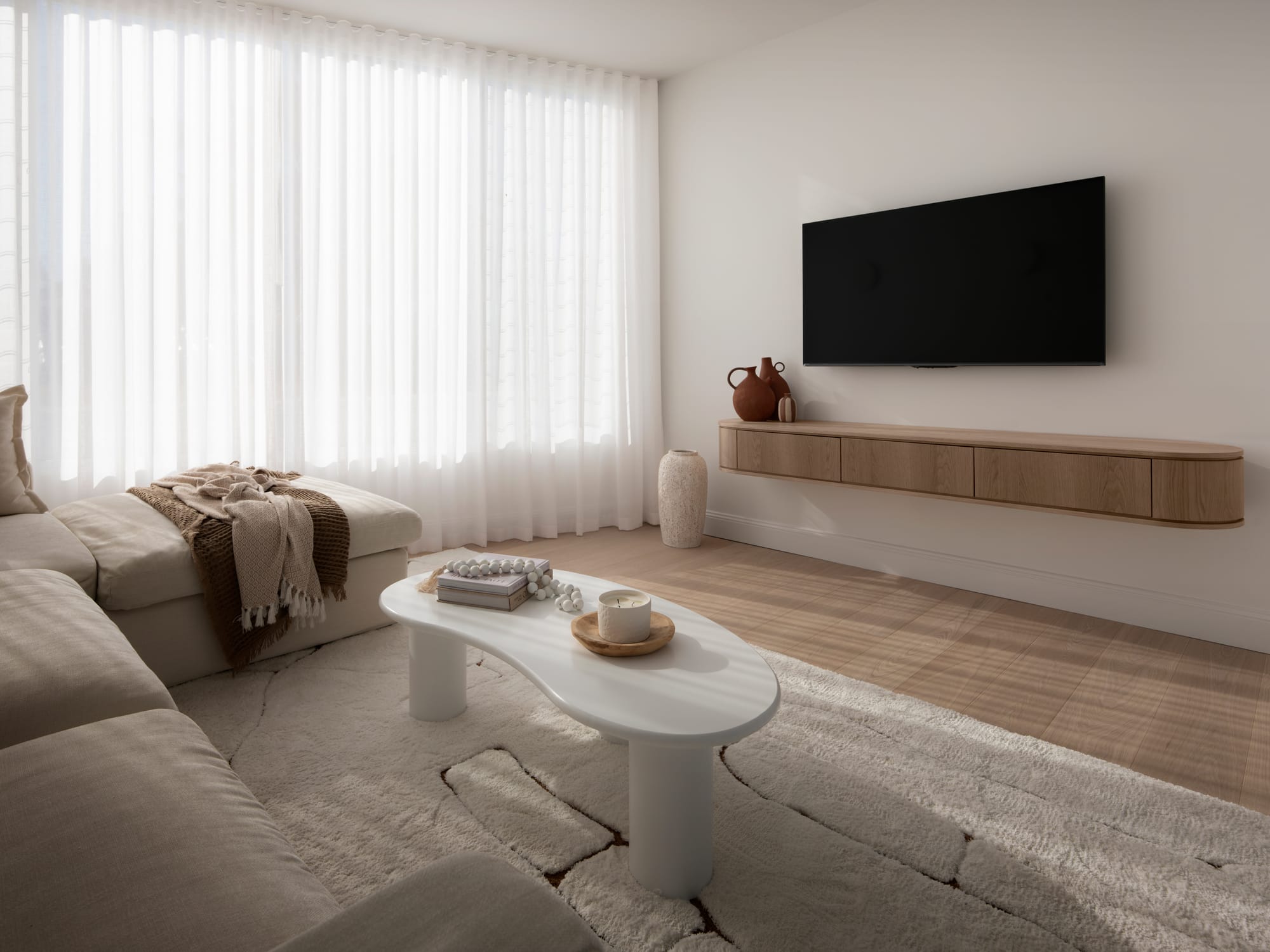 Sienna House by 868 Architects. Photography by Luke Butterly. Living space with timber floors, white sheers, white walls, beige rug, and abstractly shaped white coffee table. 