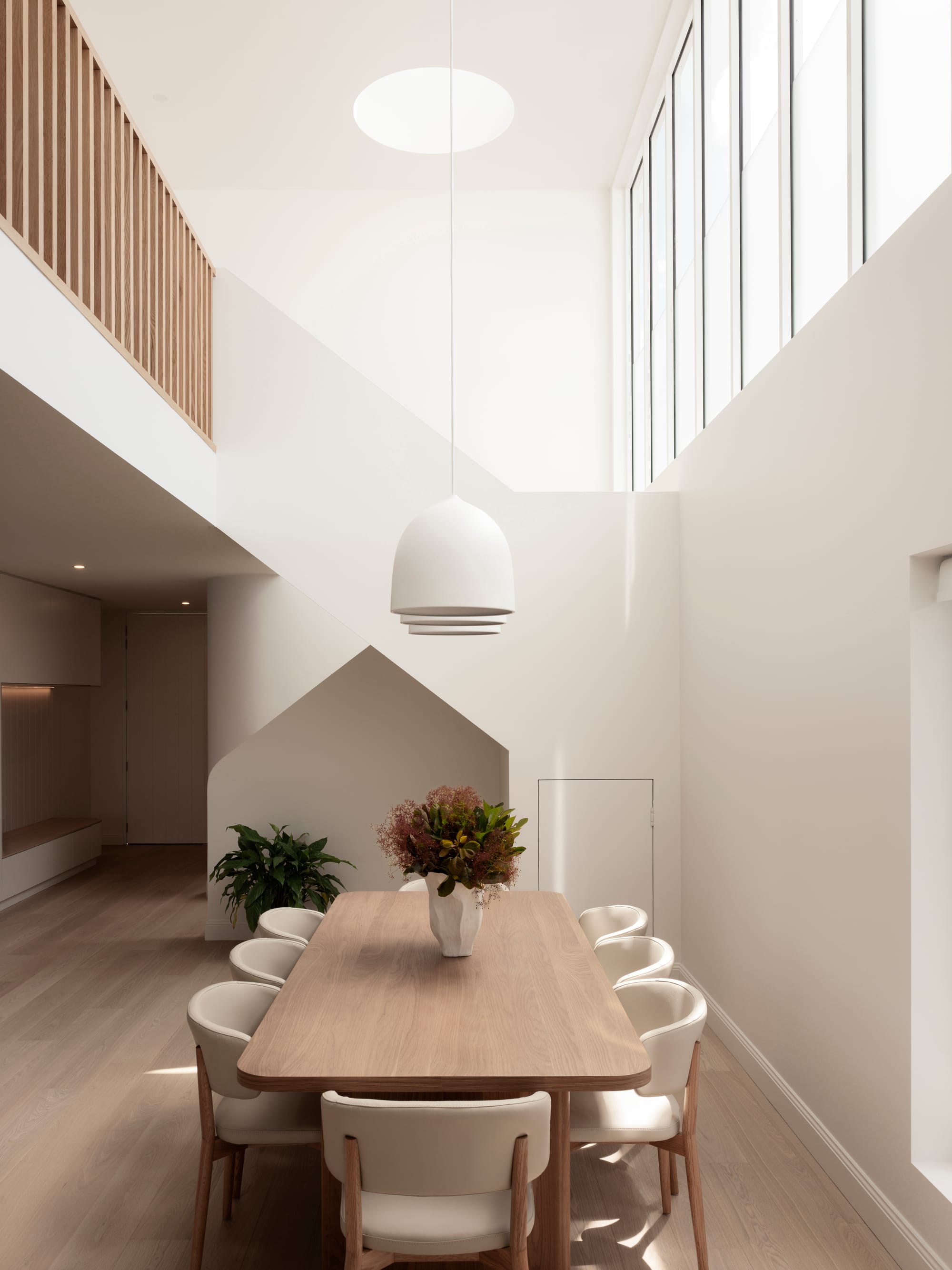 Sienna House by 868 Architects. Photography by Luke Butterly. Open plan living space with timber floor and dining table, white walls and large open void to upper level. 