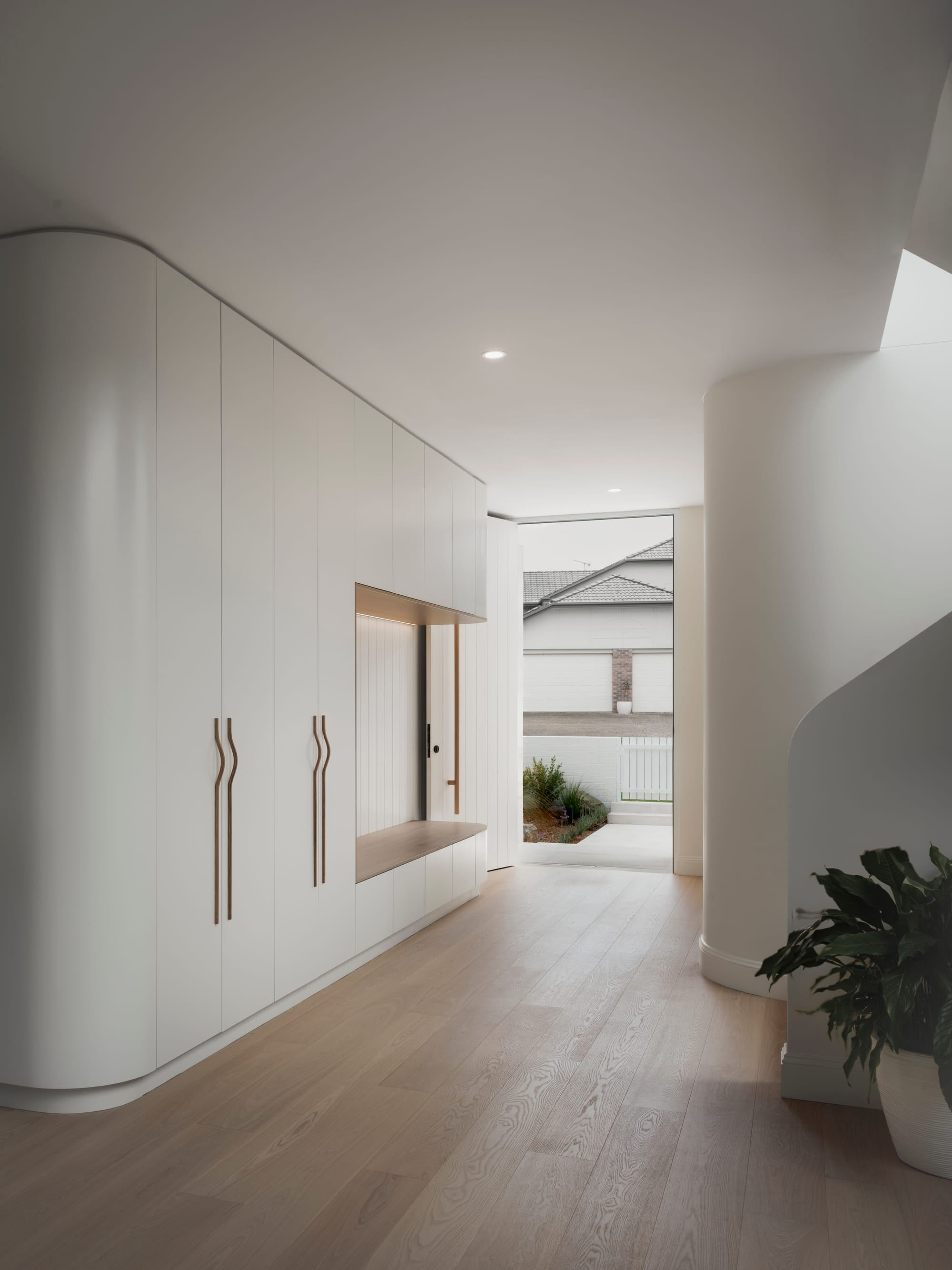 Sienna House by 868 Architects. Photography by Luke Butterly. Hallway and entry with white integrated cabinetry, timber flooring, white walls and integrated bench seating. 