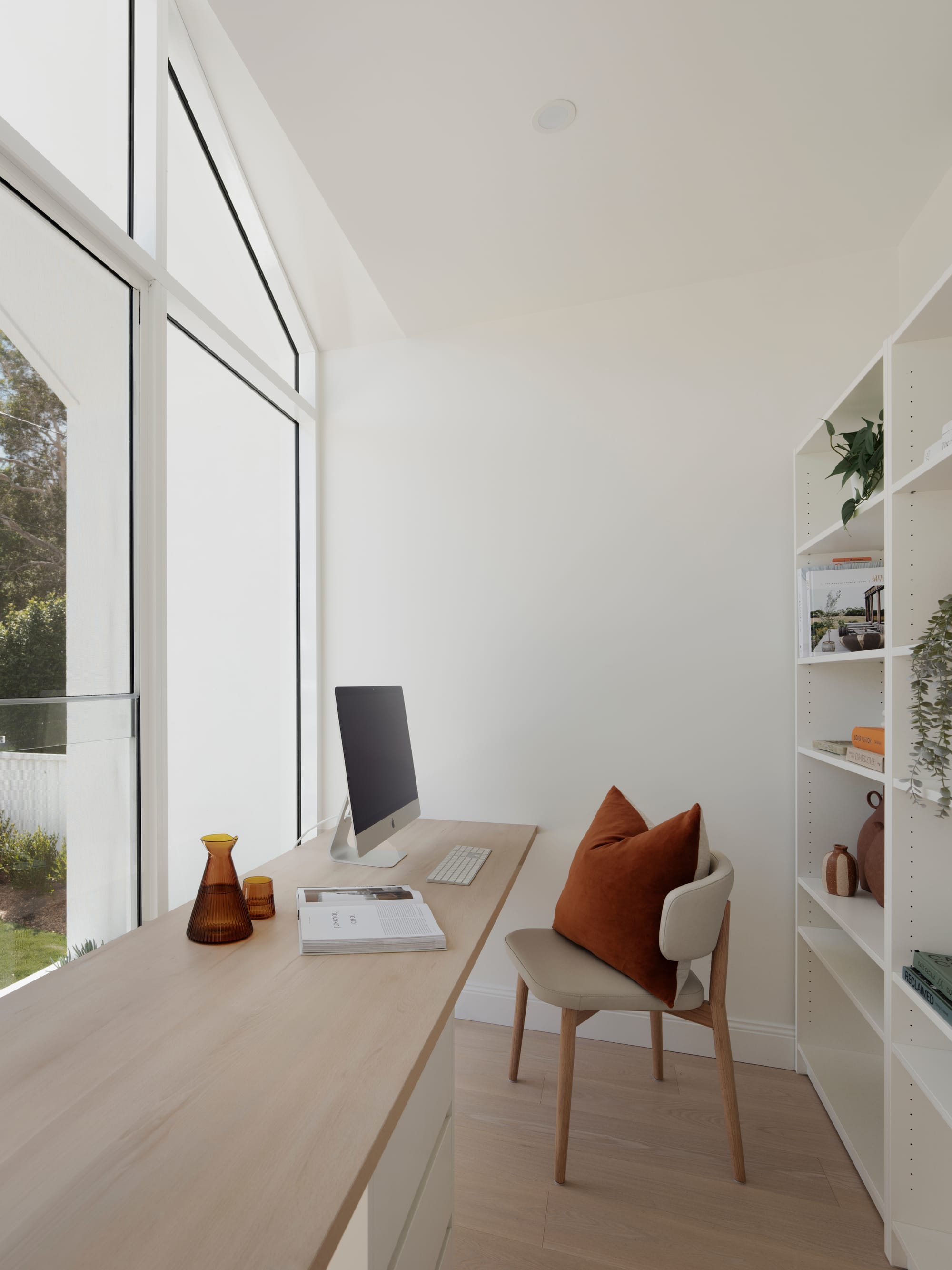 Sienna House by 868 Architects. Photography by Luke Butterly. Office space with timber flooring and timber desk, white cabinetry and walls, and windows overlooking backyard. 
