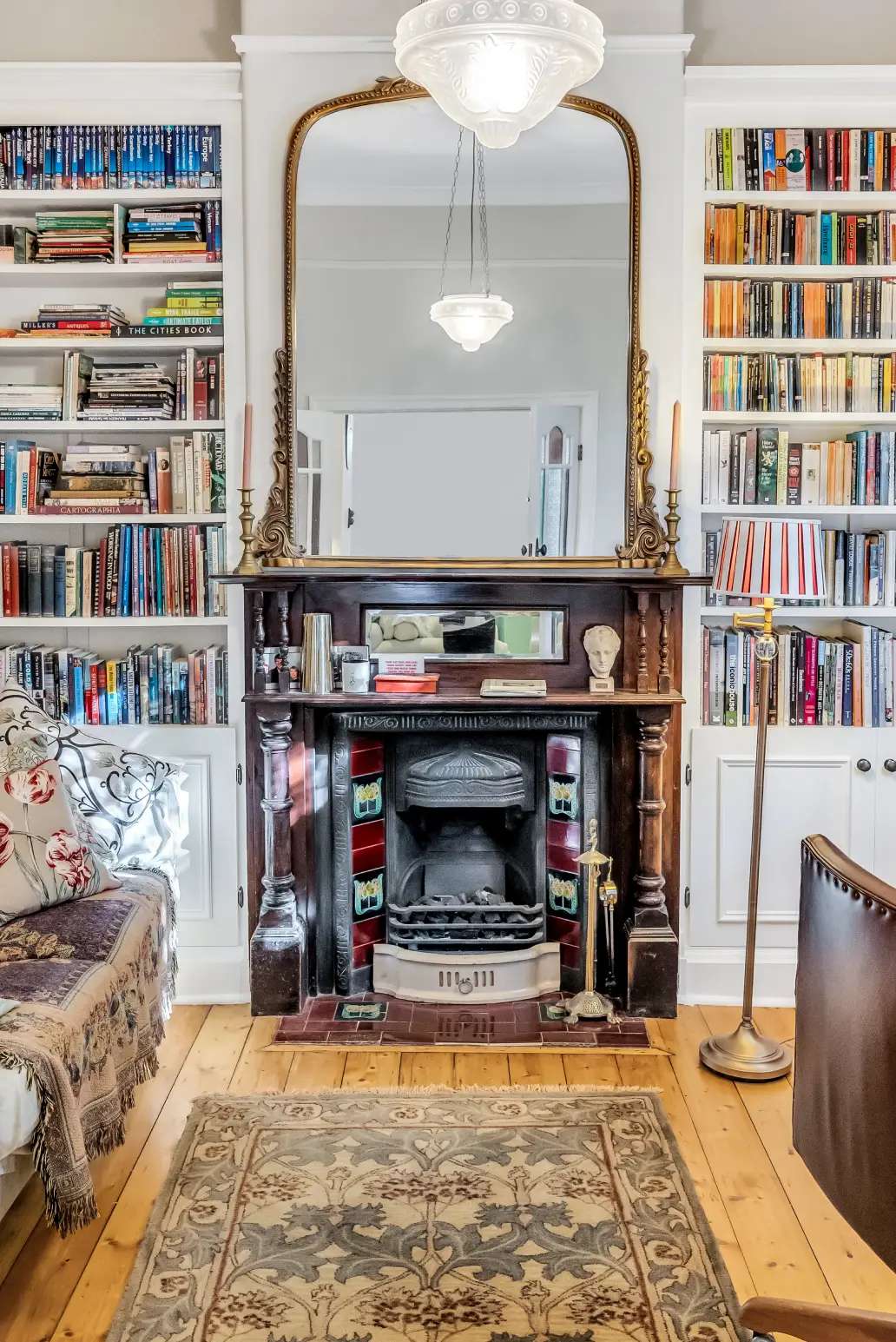 Vibrant Charm by Emotive Designs. Living room with timber floorboards, original timber fireplace, patterned rug and bookshelves. 
