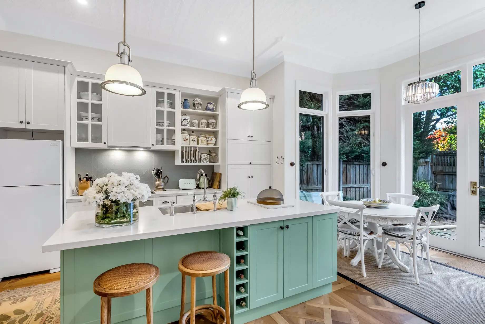 Vibrant Charm by Emotive Designs. Open plan kitchen and dining room with white and teal counters, white walls and timber flooring. 