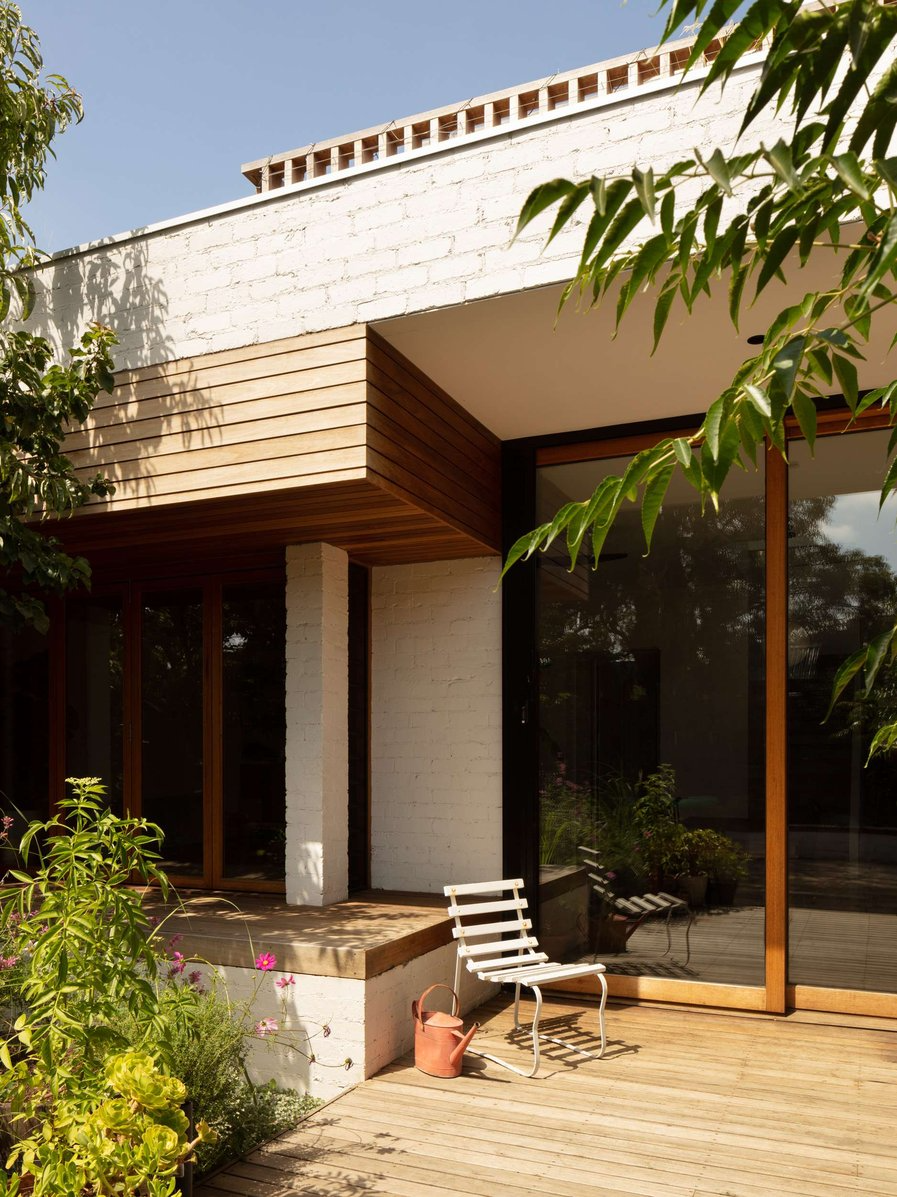 Elm Street House by Gardiner Architects. Photography by Rory Gardiner. Timber deck with white chair, white brick facade and timber framed windows.