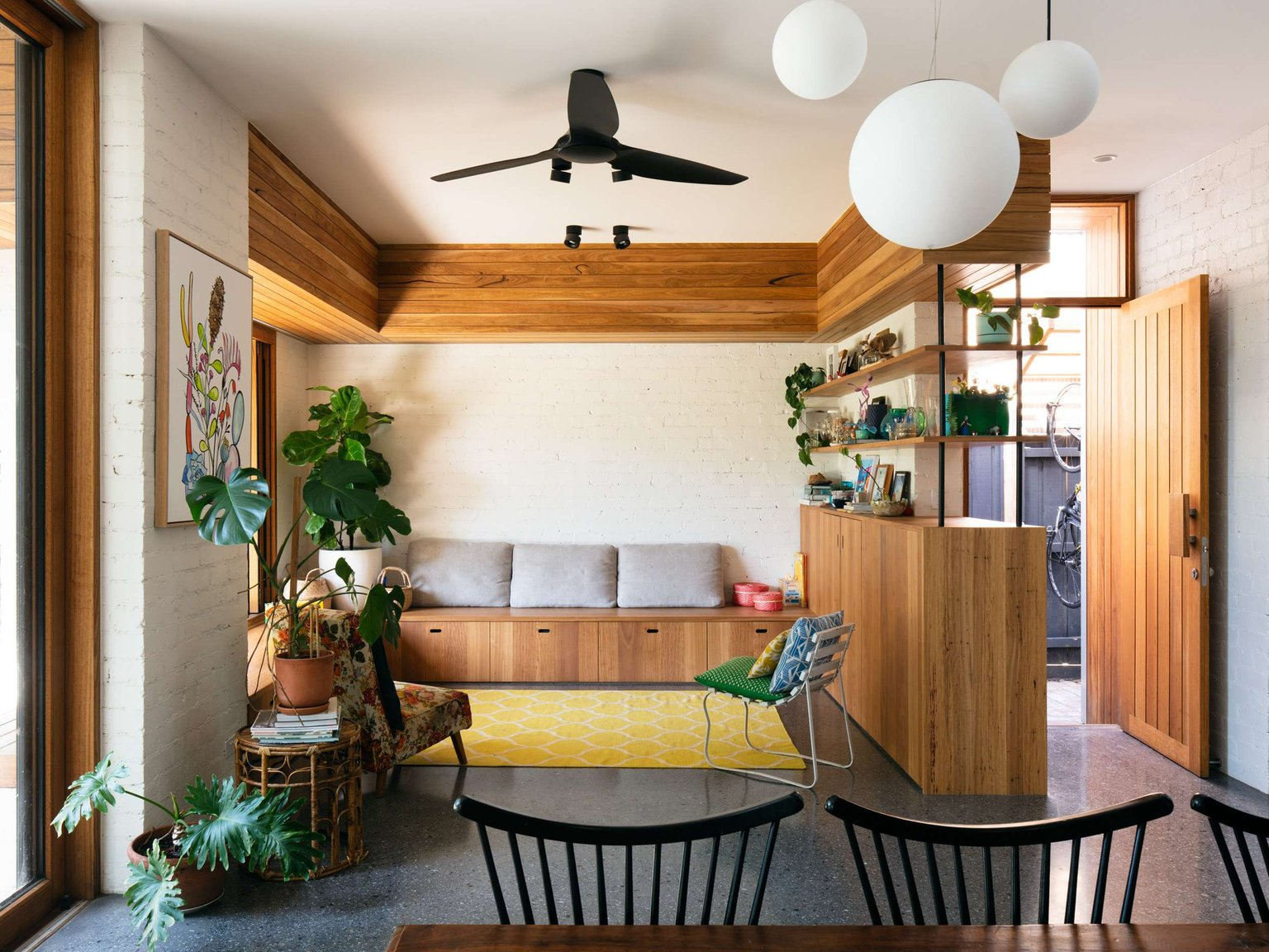 Elm Street House by Gardiner Architects. Photography by Rory Gardiner. Open plan dining and living room with concrete floors, timber joinery and yellow rug.