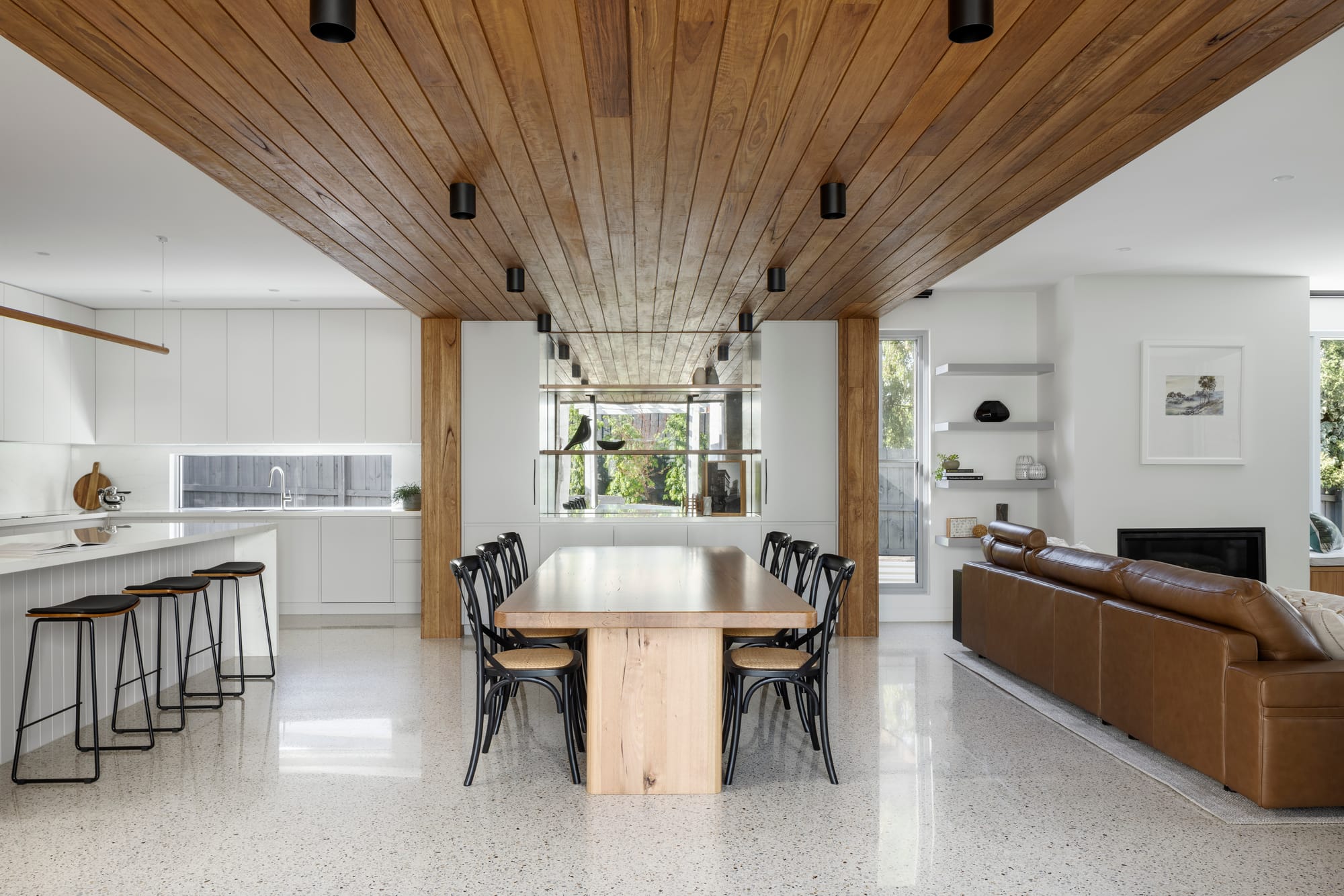 Earth + Sky House by Kirsten Johnstone Architecture. Photography by Tatjana Plitt. Open plan kitchen, dining and living space with polished concrete floors, timber clad ceiling, white walls and white cabinetry. 