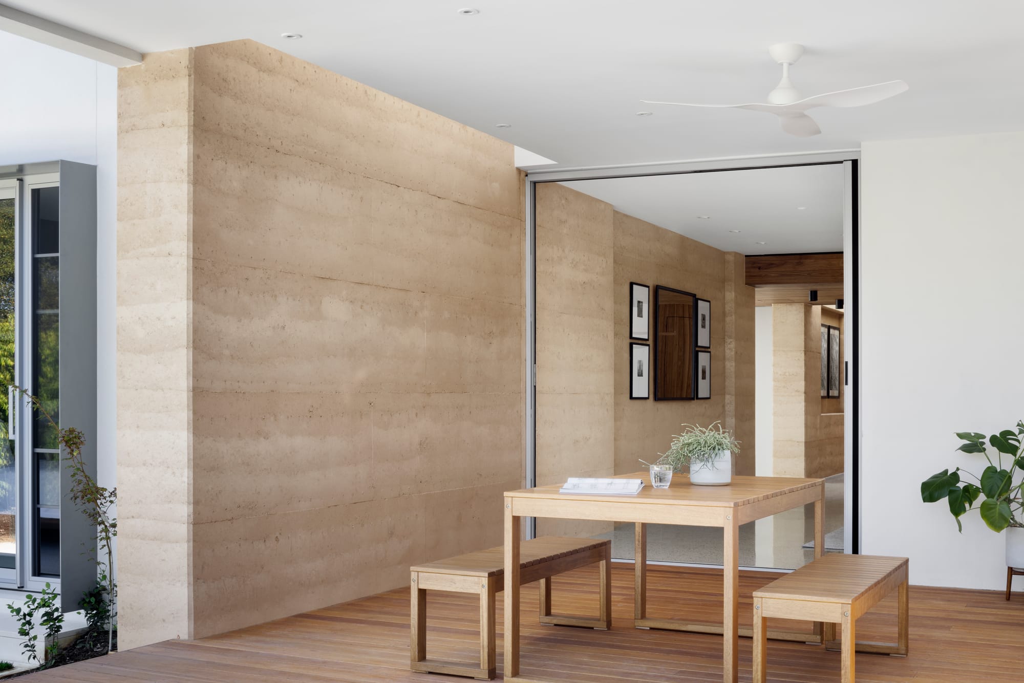 Earth + Sky House by Kirsten Johnstone Architecture. Photography by Tatjana Plitt. Outdoor timber deck with large double door access to interior, rammed earth and white walls and timber dining table. 