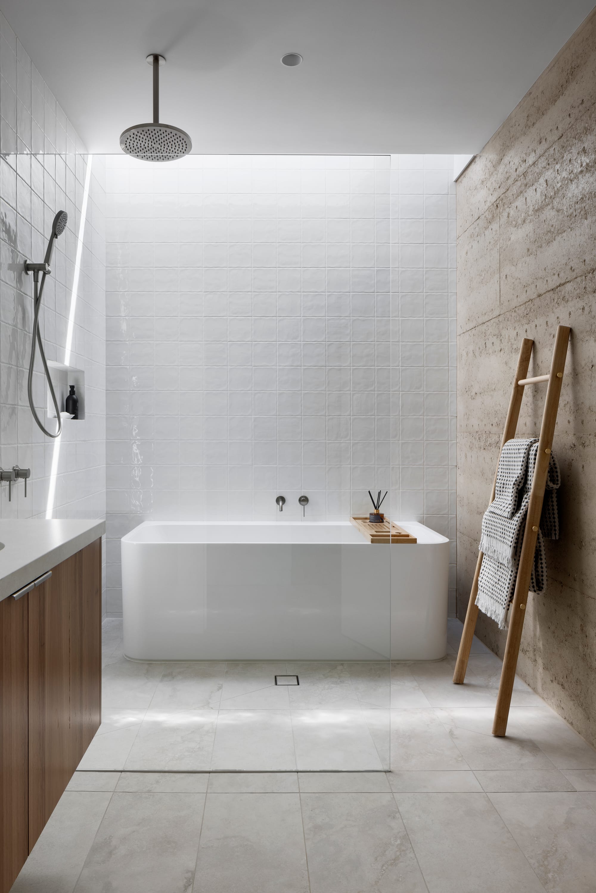 Earth + Sky House by Kirsten Johnstone Architecture. Photography by Tatjana Plitt. Bathroom with grey tile flooring, rammed earth and white tile walls, timber cabinetry, glass screen and freestanding white tub. 