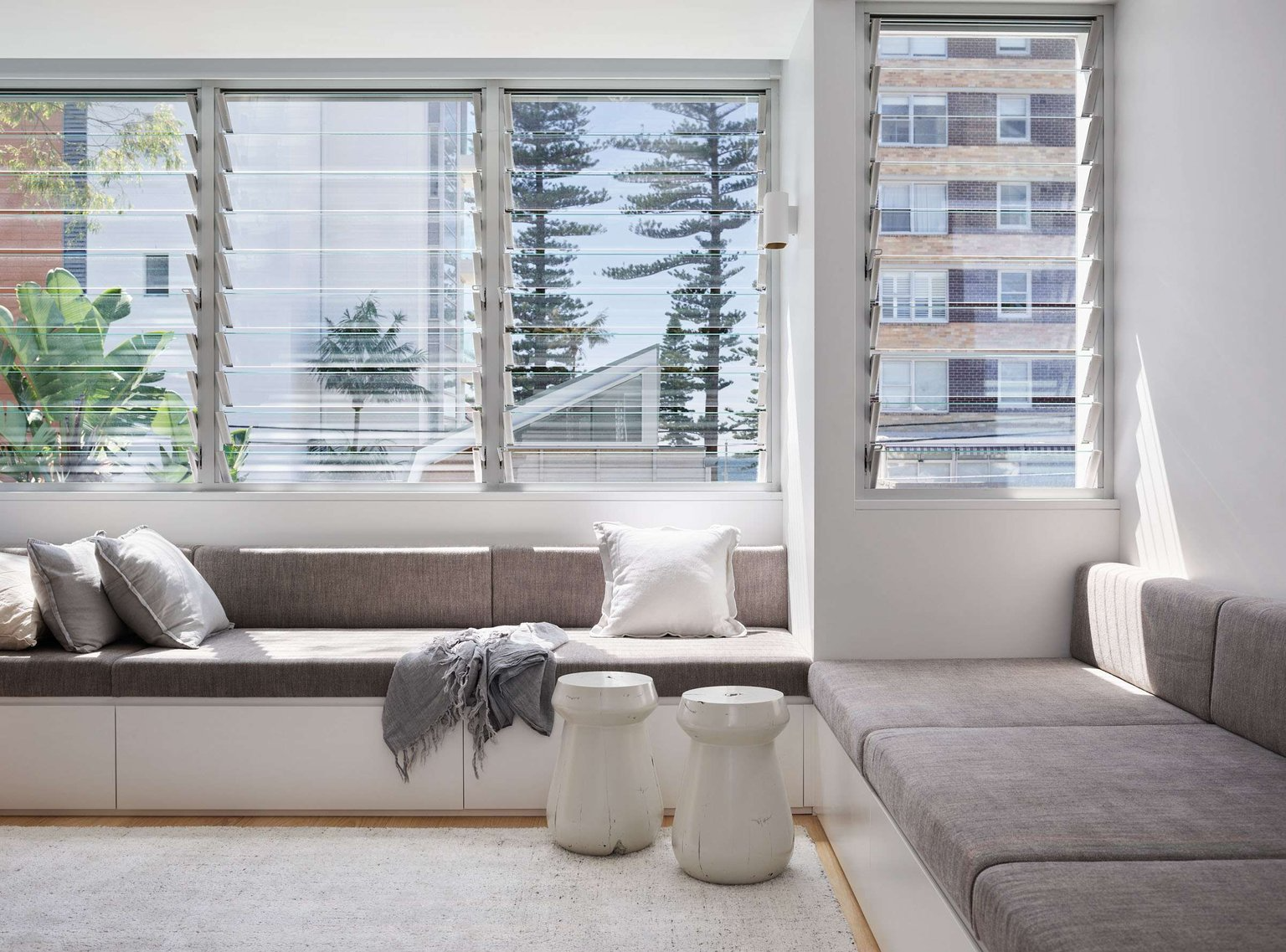 Manly 22 by Watershed Architects. Photography by Alicia Taylor Photography. Living space with louvre glass shutters overlooking city views, with a built-in grey and white window bench.