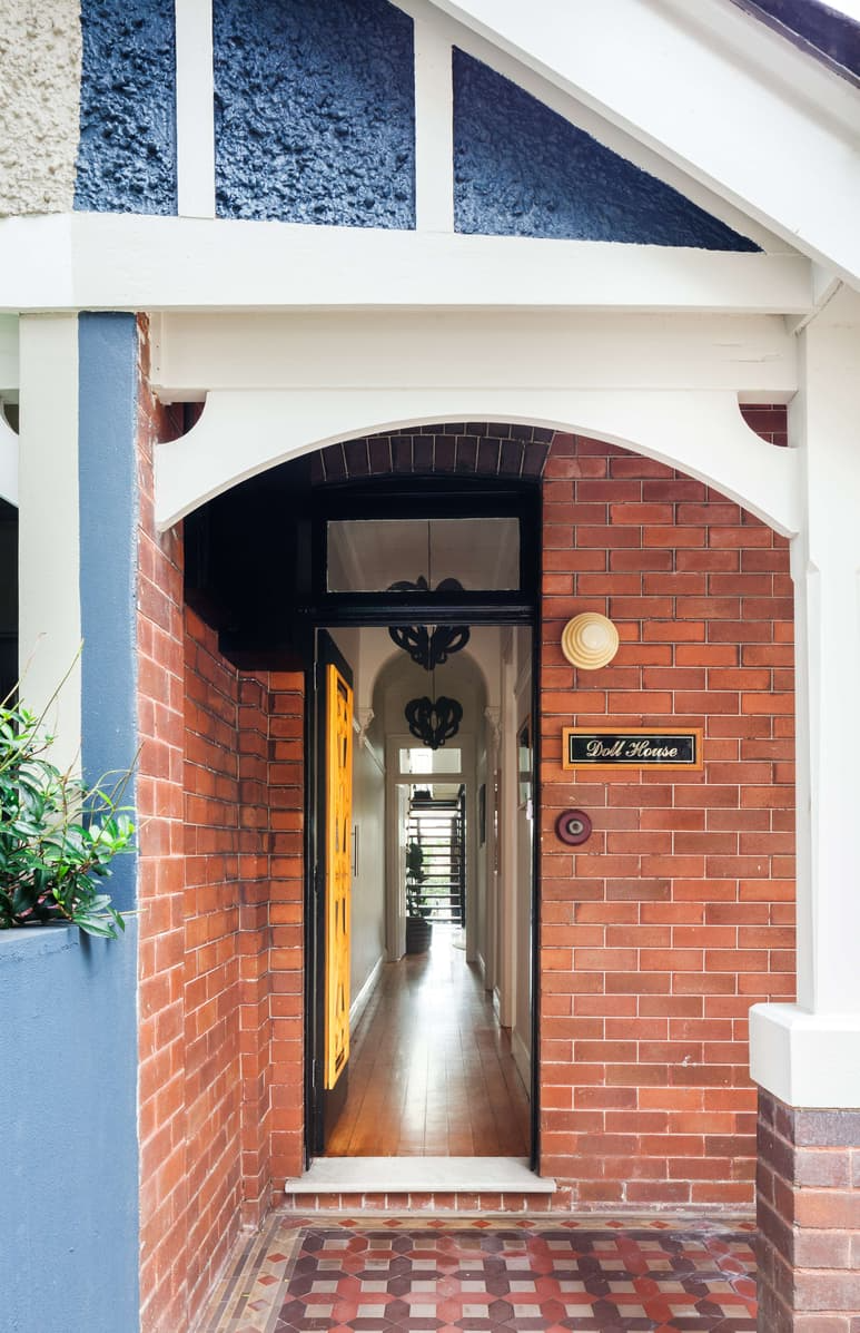 Randwick by Matt Day Architect. Photography by Katherine Lui. Exterior entry of home with red brick walls, patterned tiled floors, blue rendered retaining wall and yellow front door.