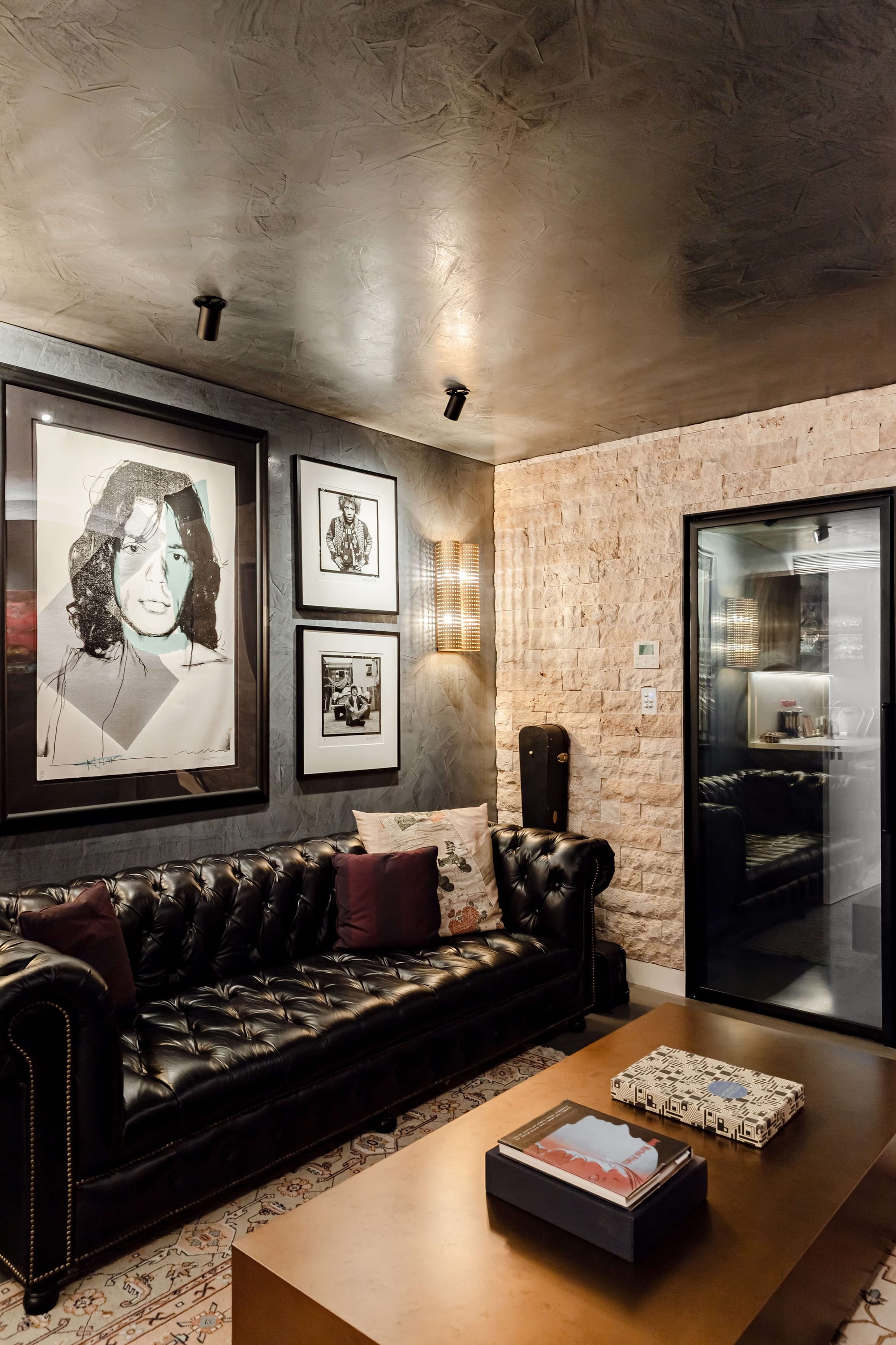 Avalon Beach Wine Cellar & Lounge by Nx Studio. Photography by REM Design House. Black leather couch with brass coffee table on patterned rug in front of stone wall. 