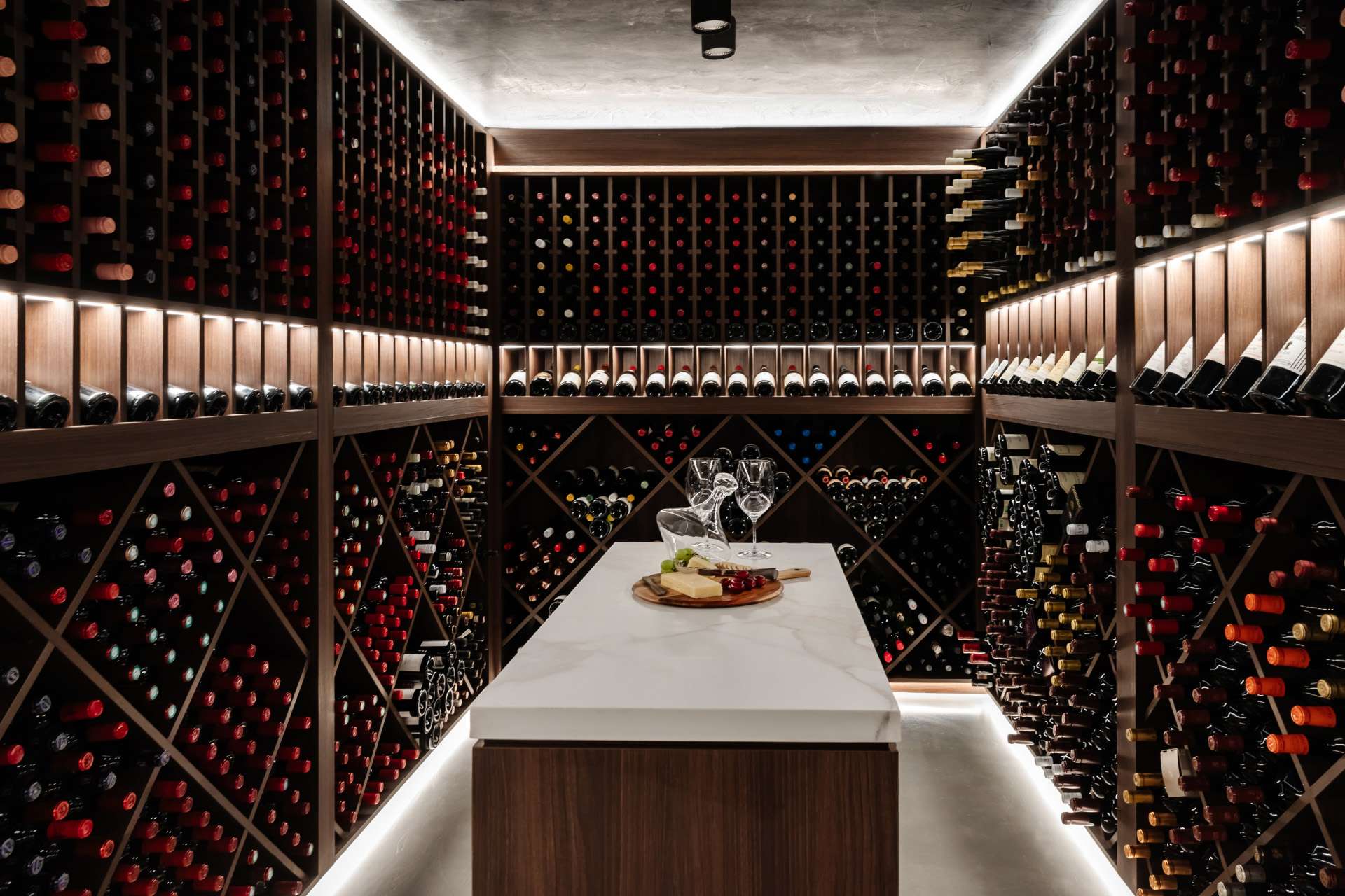 Avalon Beach Wine Cellar & Lounge by Nx Studio. Photography by REM Design House. Cellar with three walls covered with timber wine bottle storage, and a timber and marble island in centre. 