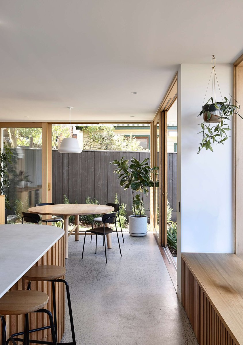 Brooke by Ola Architecture Studio. Photography by Derek Swalwell. Open plan dining and kitchen with concrete flooring, timber joinery and dining table, and sliding doors onto garden.