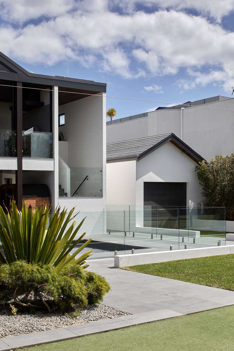 Bay View House by Samuel Architecture. Photography by Dave Kulesza. Exterior rear facade of double storey modern home with glass fence, grey pavers and grass. 