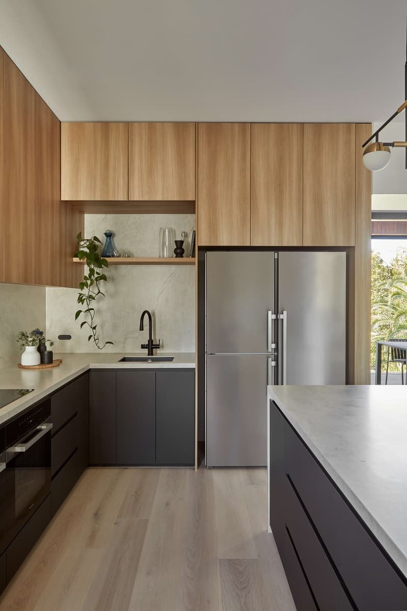 Horizon Home by Samuel Architecture. Photography by Dave Kulesza. Kitchen with black and timber cabinetry, chrome appliance, and stone countertop and splashback. 
