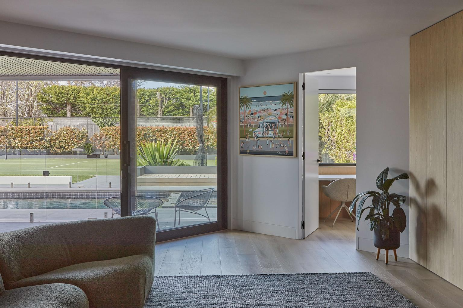 Horizon Home by Samuel Architecture. Photography by Dave Kulesza. Interior with timber flooring, white walls, beige couch and windows overlooking outdoor pool and tennis court. 