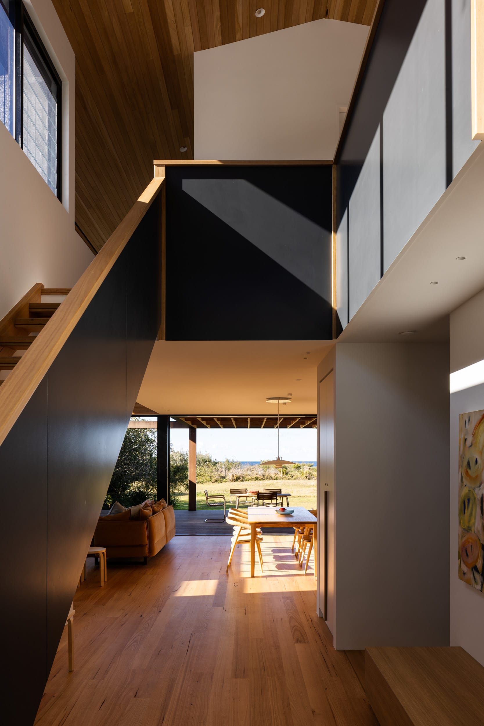 Bawley Point by Watershed Architects. Photography by Simon Whitbread. Internal entry with black staircase balustrade, and timber flooring leading through to open plan dining and living area. 