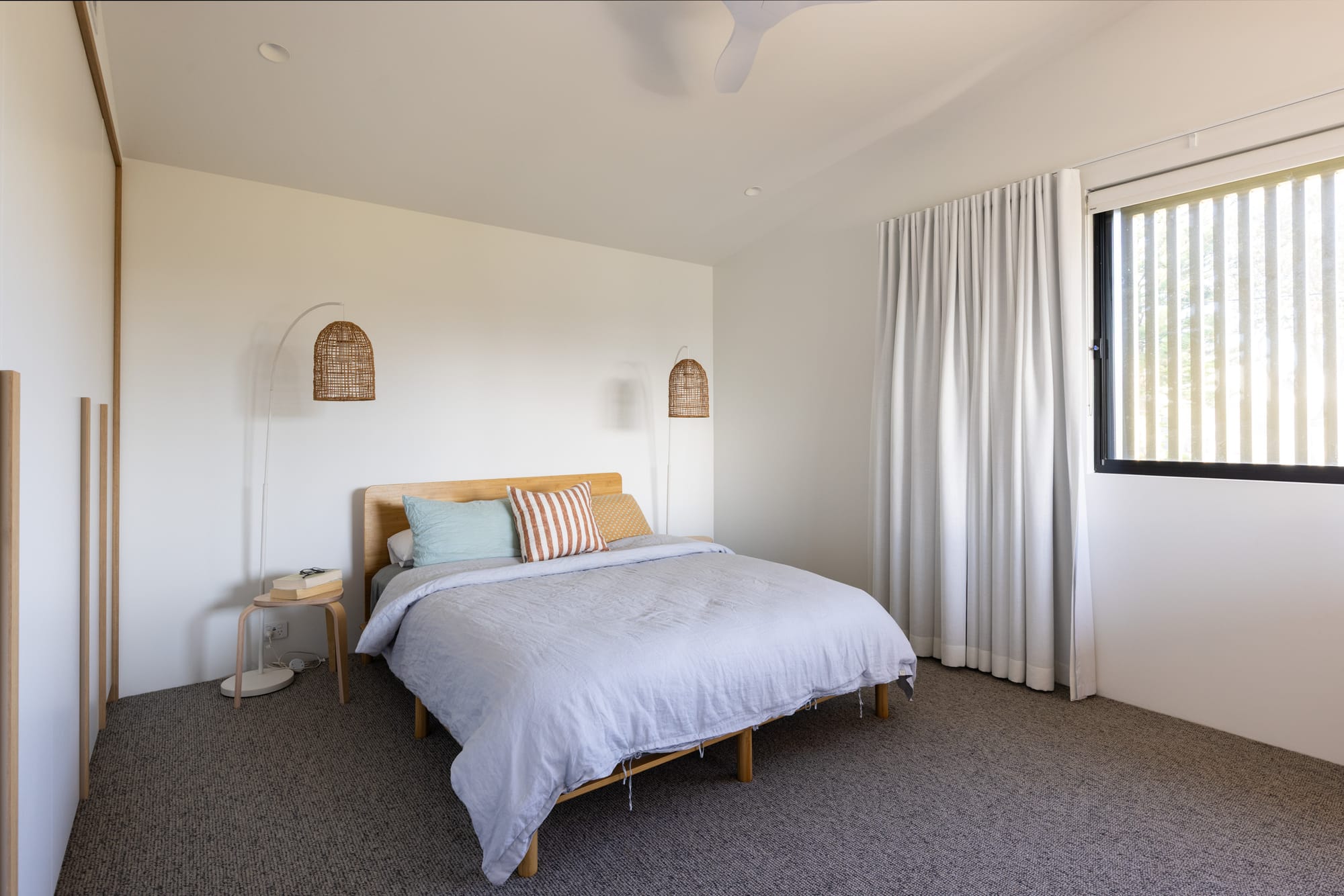 Bawley Point by Watershed Architects. Photography by Simon Whitbread. Bedroom with white walls, grey carpets, timber bedframe, rattan floor lamps and light grey bedding. 