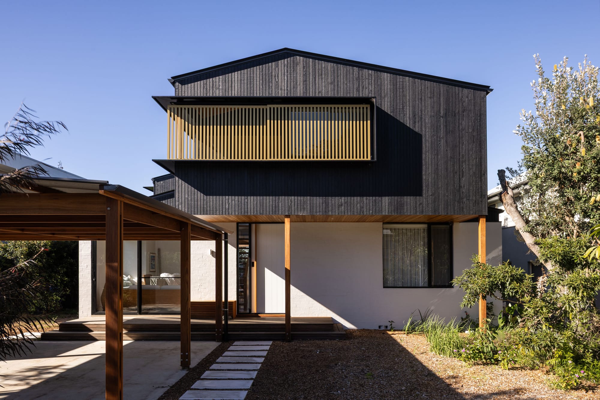 Bawley Point by Watershed Architects. Photography by Simon Whitbread. Front facade of double-storey home with white brick facade on first floor, charcoal timber clad upper level, and exposed timber structure for garage to the left. 