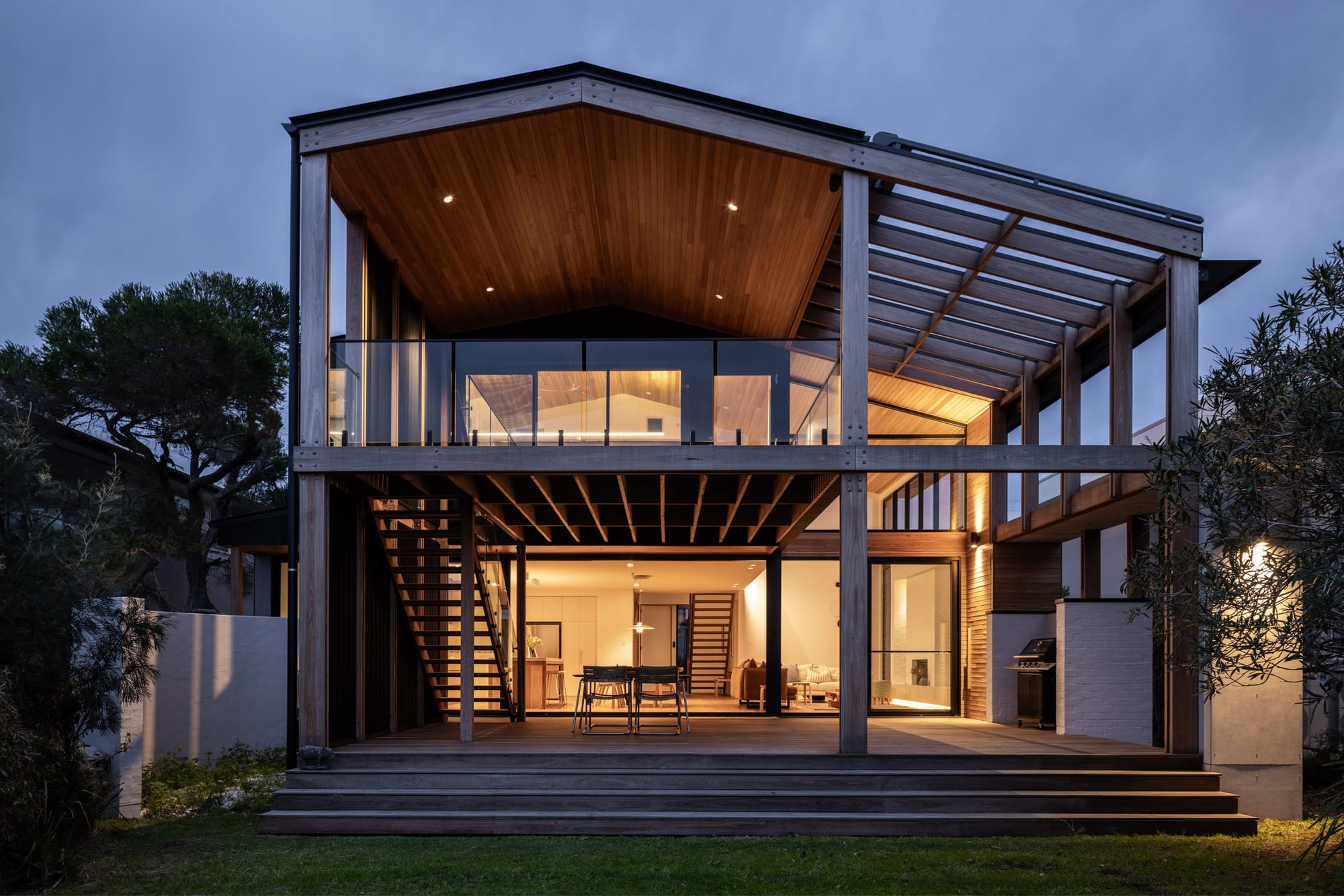 Bawley Point by Watershed Architects. Photography by Simon Whitbread. Rear facade of contemporary doule-storey home at night, with warm interior light visible through large glass openings. 