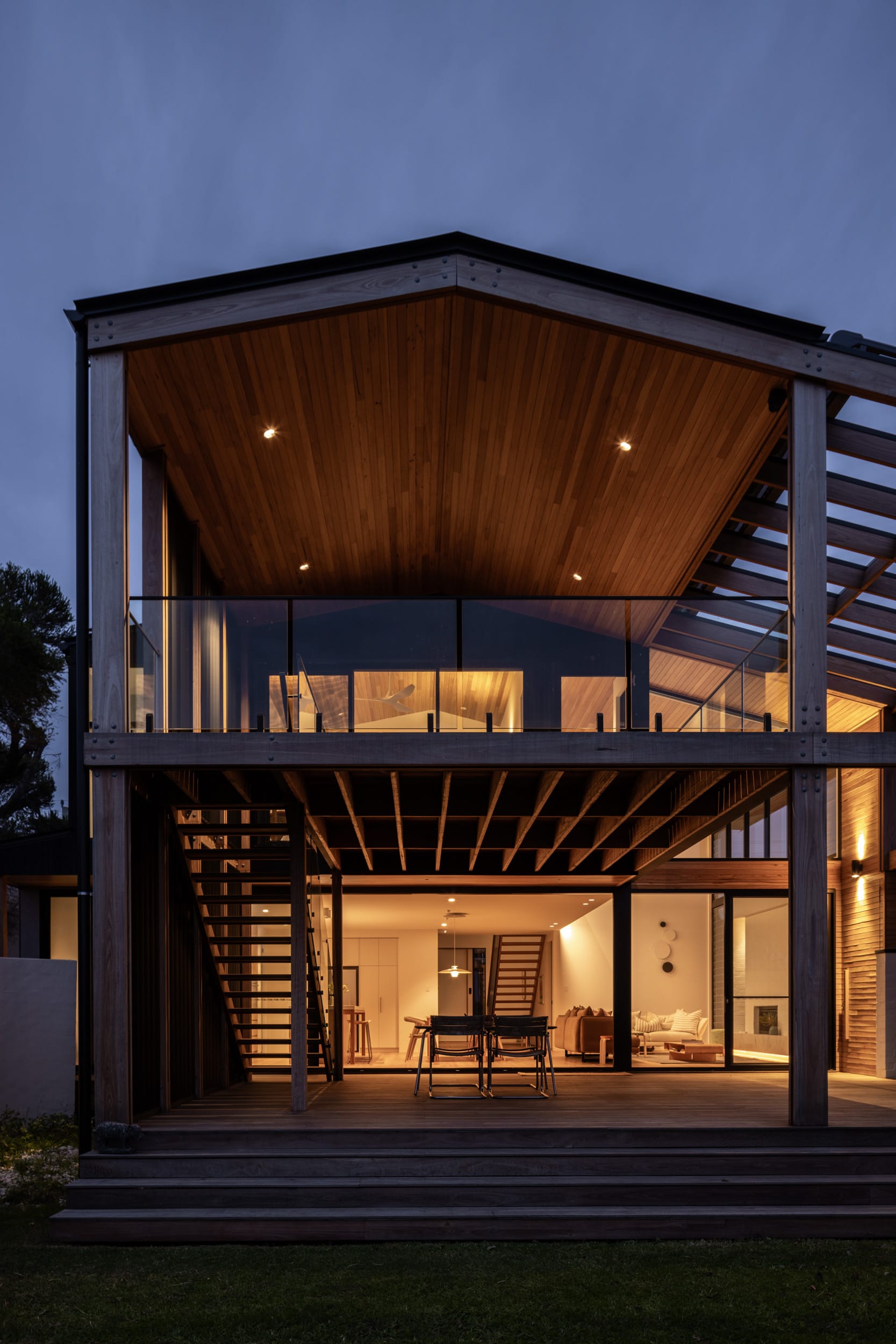 Bawley Point by Watershed Architects. Photography by Simon Whitbread. Rear afacde of home with timber deck on bottom level, balcony on upper level and light emitting from interior. 