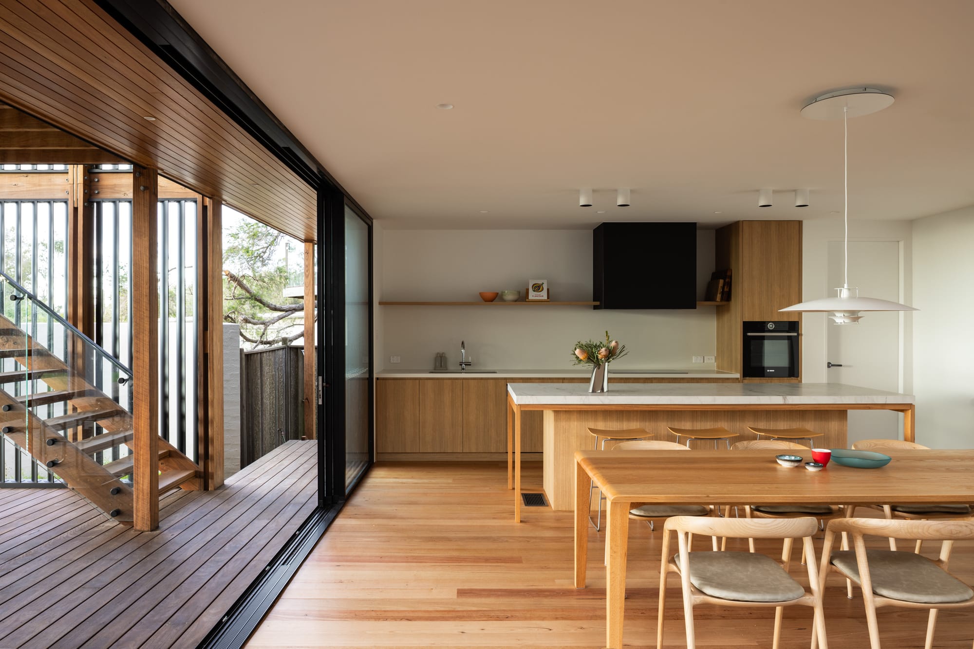 Bawley Point by Watershed Architects. Photography by Simon Whitbread. Open plan kitchen and dining space opening onto external timer deck via large black and glass sliding doors.