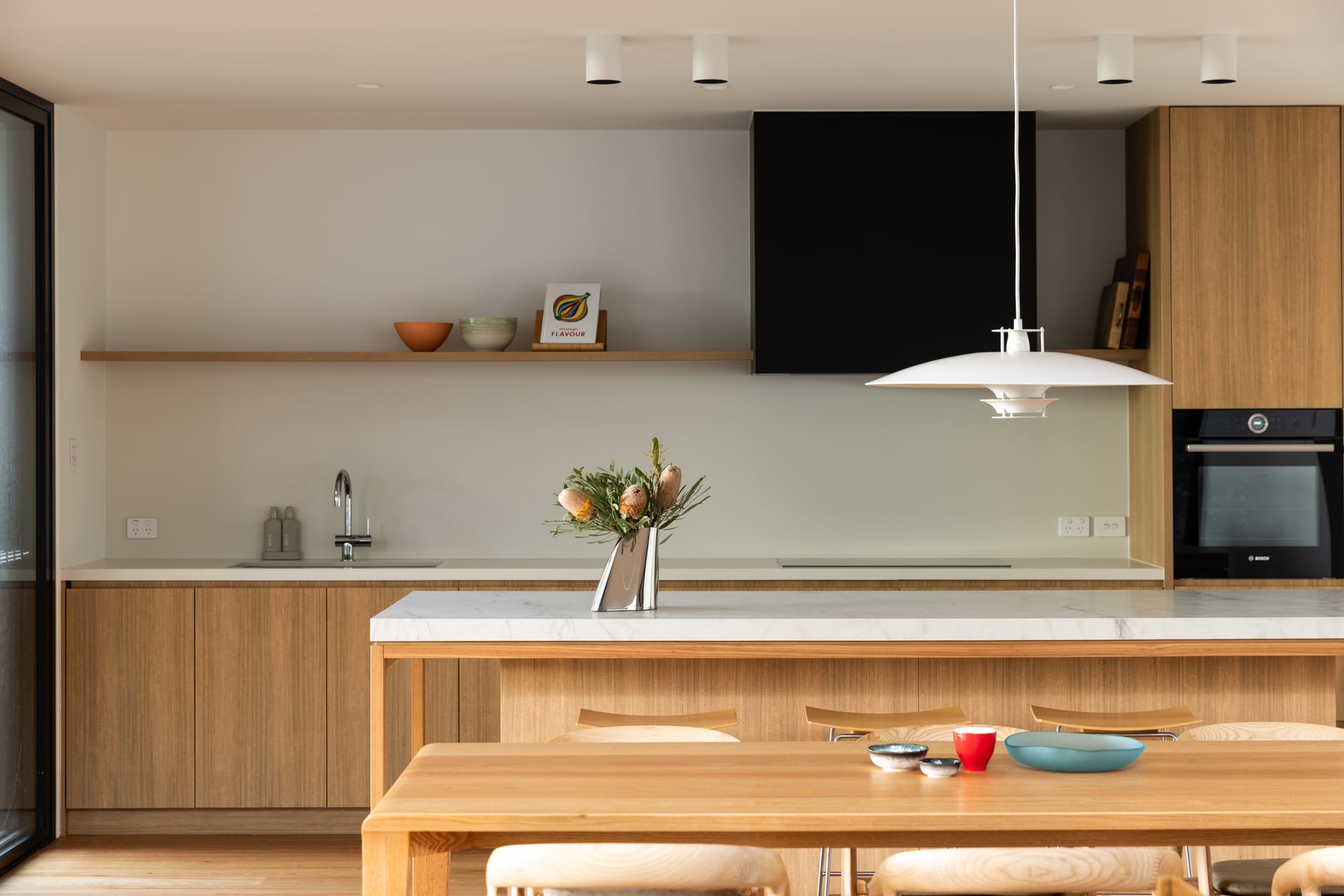 Bawley Point by Watershed Architects. Photography by Simon Whitbread. Kitchen with timber cabinetry, white stone benchtops, white walls, black appliances and rangehood. 