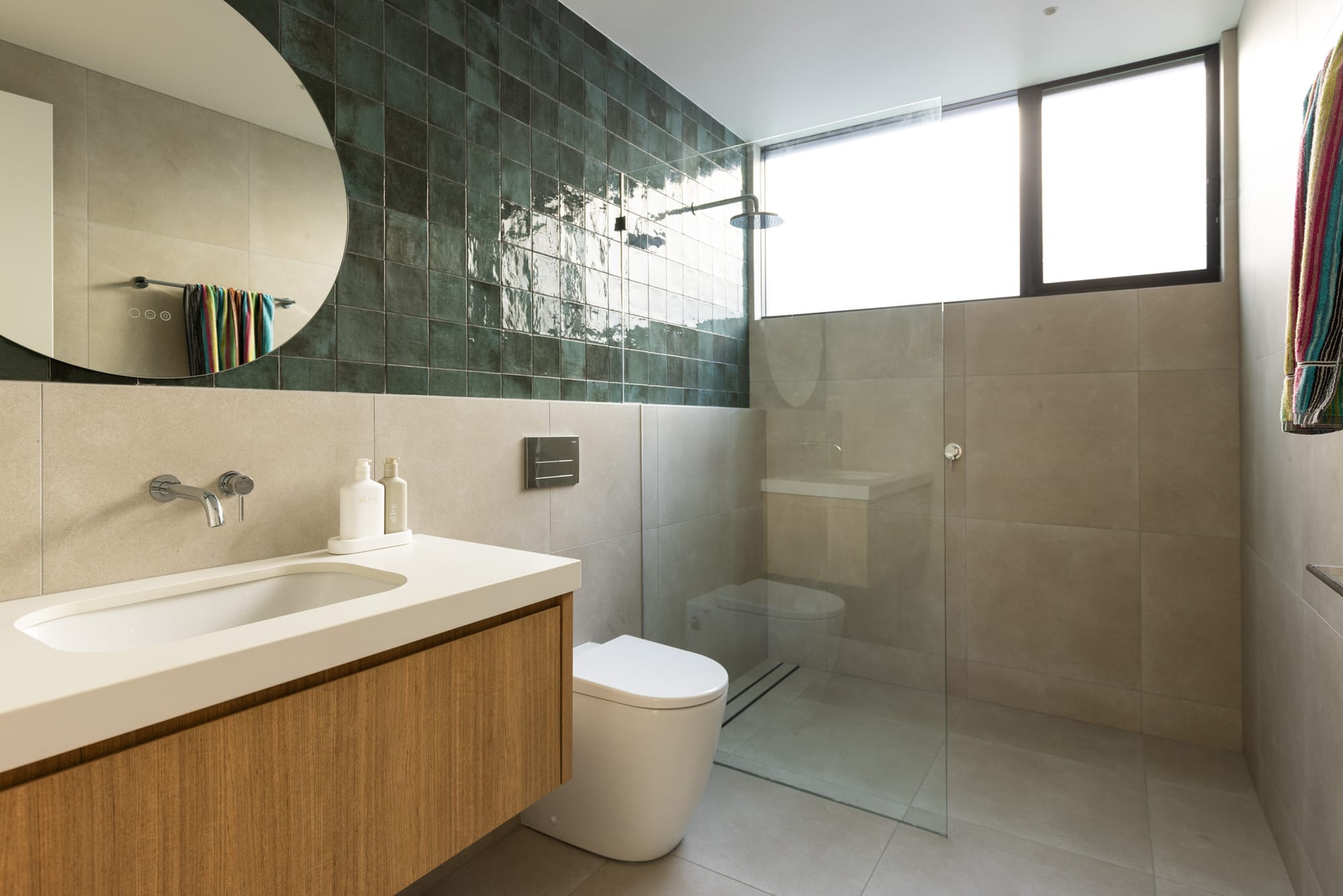 Bawley Point by Watershed Architects. Photography by Simon Whitbread. Bathroom with grey floor and wall tiles, moss green tiled splashback, timber cabinetry, and glass shower screen. 