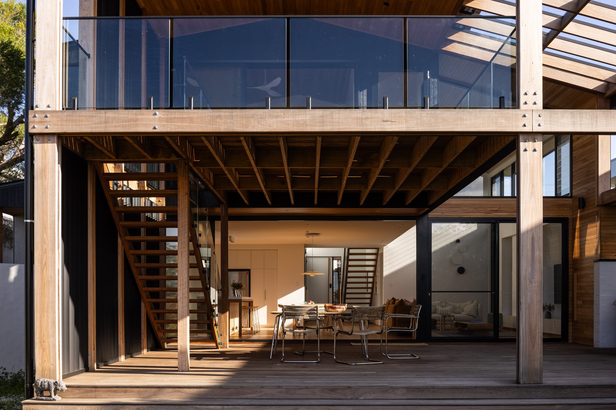 Bawley Point by Watershed Architects. Photography by Simon Whitbread. Rear facade of home with timber deck, balcony on upper floor with glass balustrade, double height timber pillars and exposed timber ceiling. 