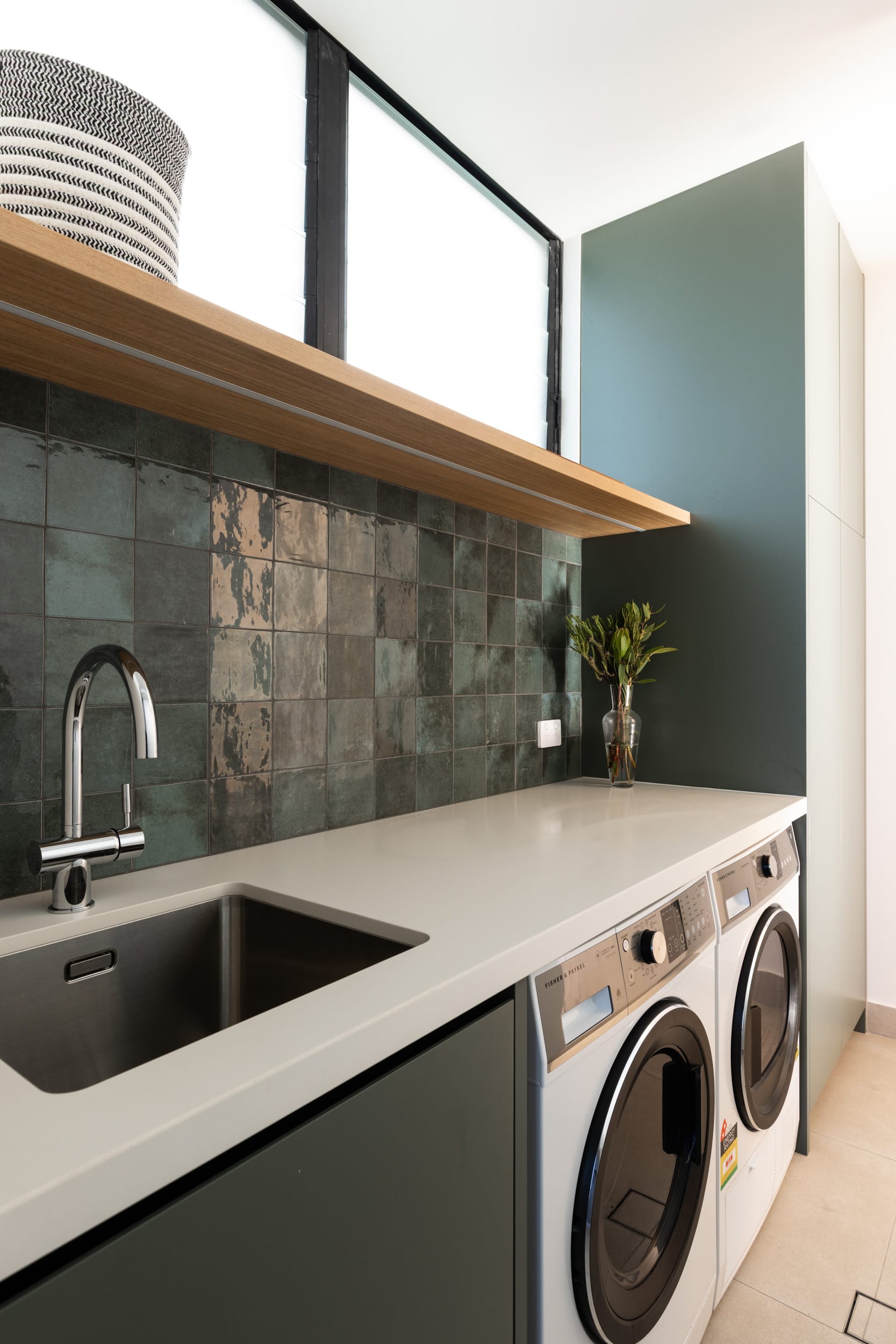 Bawley Point by Watershed Architects. Photography by Simon Whitbread. Laundry with moss green splashback tile, white countertop, black cabinetry, white appliances and exposed timber shelving.  