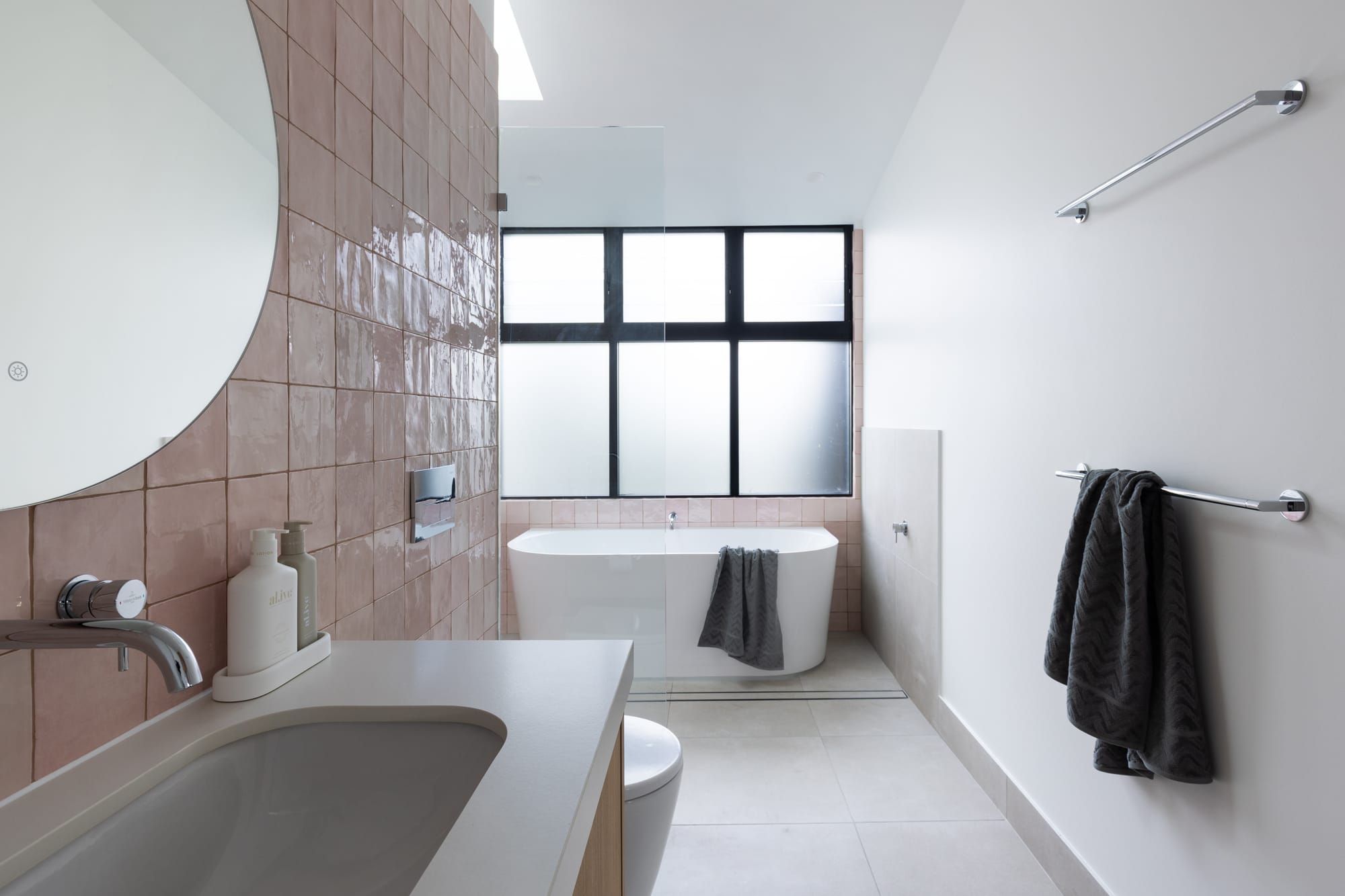 Bawley Point by Watershed Architects. Photography by Simon Whitbread. Bathroom with pink tiled splashback, white floor tiles and white walls, freestanding white tub and white countertops. 