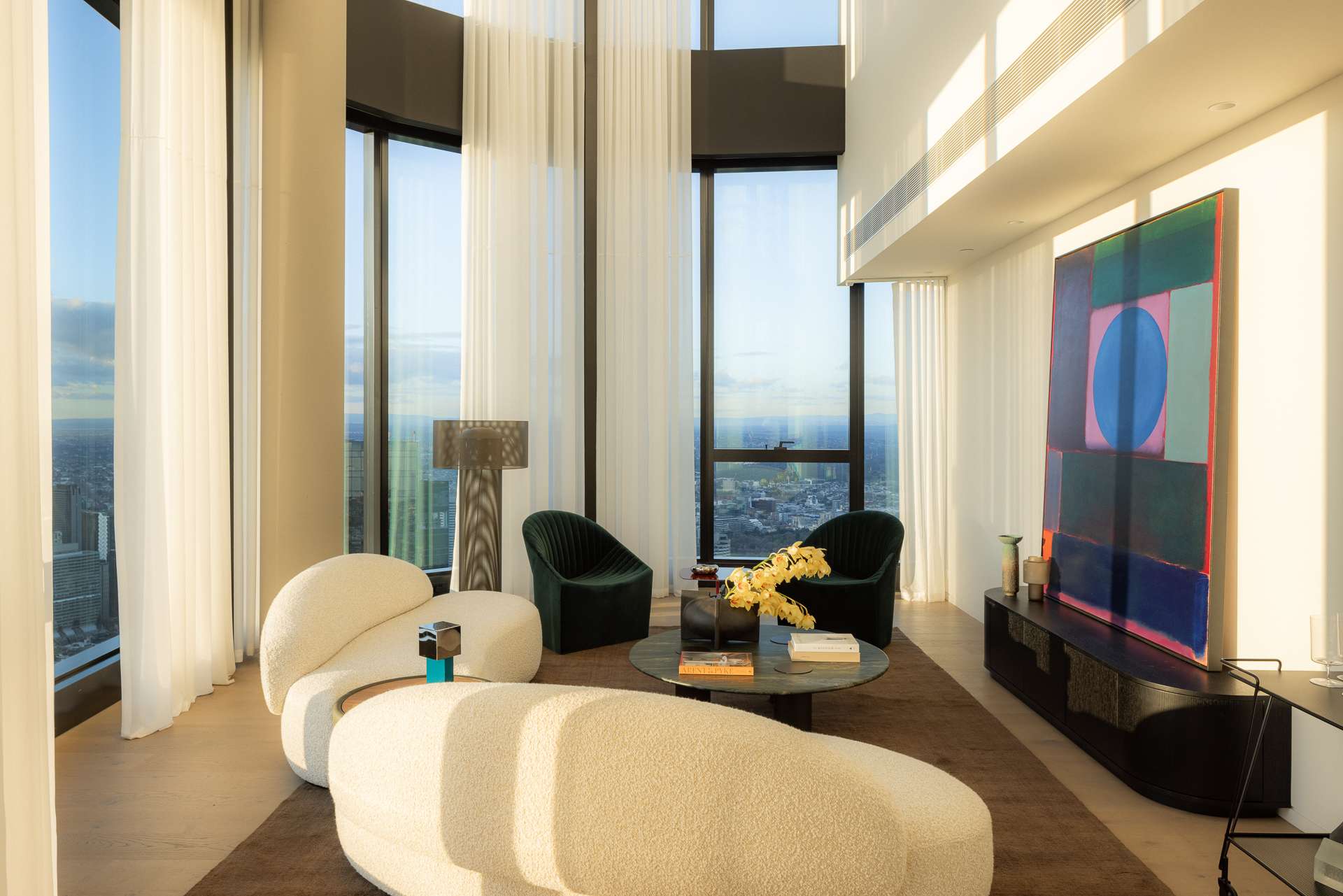 Cloud Residence by FURNISHD. Photography by Dylan James. Living space with full-height windows and white sheers, white boucle couches, forest green armchairs, white walls, abstract art.